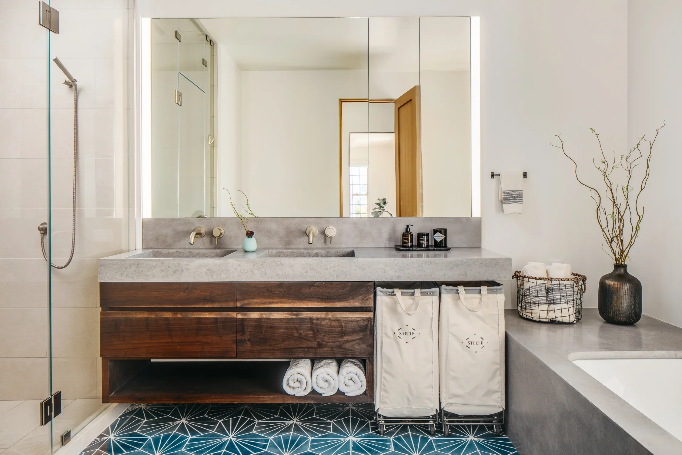 Primary bathroom with double concrete sink vanity, dark walnut cabinetry, backlit medicine cabinet mirror, blue geometric cement tile floor, and concrete soaking tub surround — Mission Loft San Francisco by Mokume Design Studio