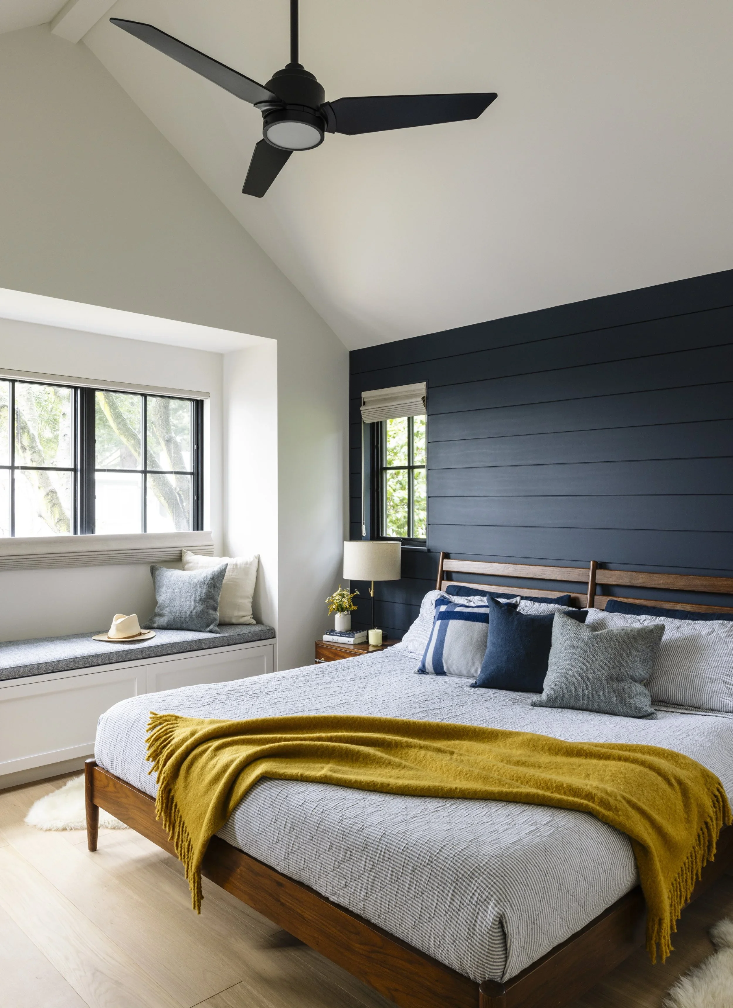 Primary bedroom with navy painted shiplap accent wall, walnut platform bed, mustard yellow throw, built-in window seat, and vaulted ceiling with black ceiling fan — Corte Madera Residence by Mokume Design Studio
