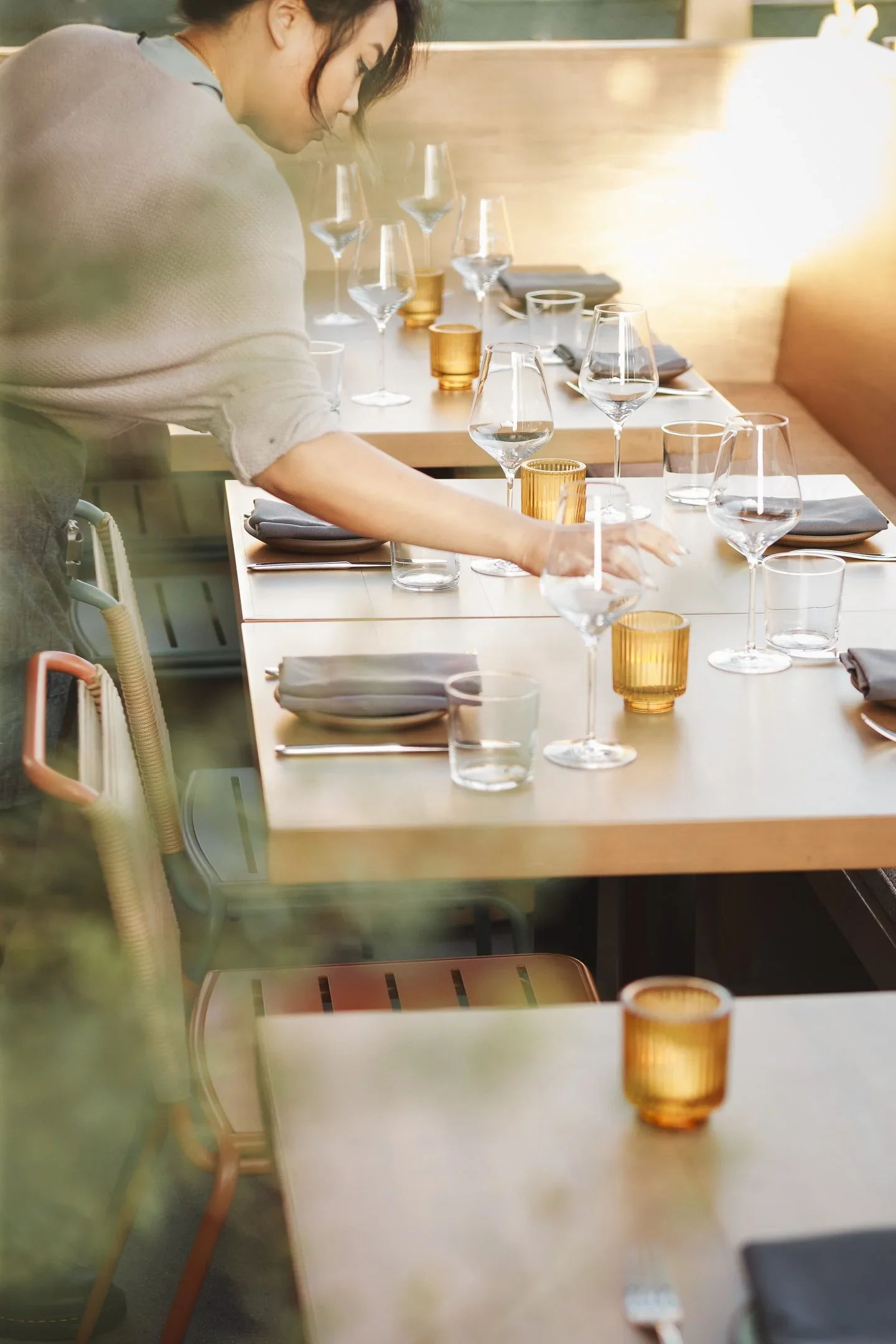 Server setting a table at a teal slatted banquette beneath a wood louver screen with garden views — Marlena restaurant interior design Long Beach by Mokume Design Studio