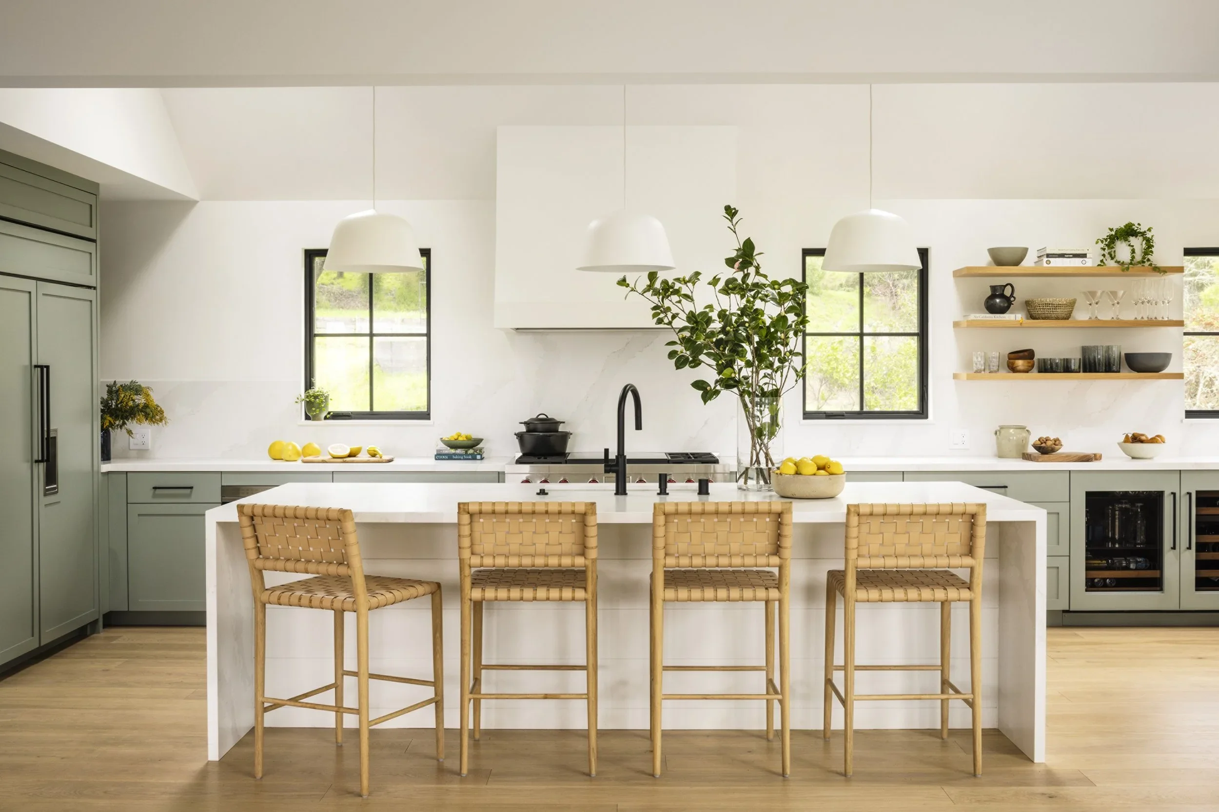 Sage green shaker kitchen with white quartz island, woven leather barstools, open oak shelving, wine fridge, and breakfast nook beyond — Corte Madera Residence by Mokume Design Studio