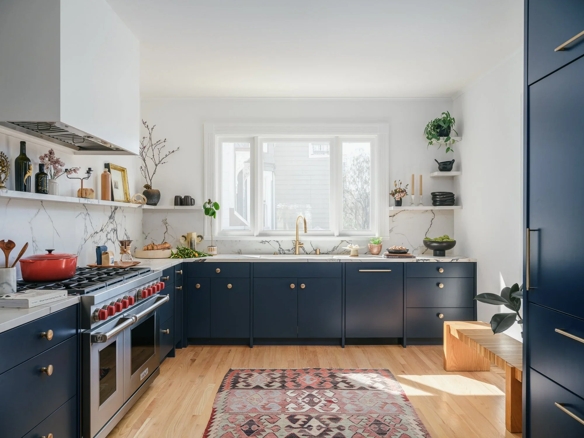 Navy blue shaker kitchen with Calacatta marble backsplash, Wolf professional range, brass hardware, open shelving, and Kilim rug on wide plank hardwood floors — Hill Street Residence San Francisco by Mokume Design Studio