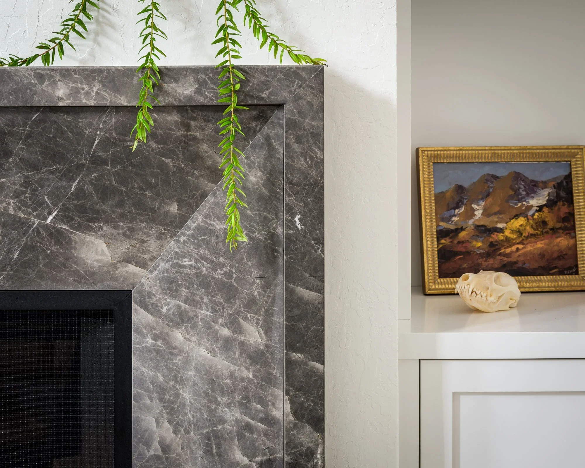 Close-up of gray marble fireplace surround with mitered stone corners and trailing greenery beside styled white built-in shelving — Pacific Heights San Francisco by Mokume Design Studio