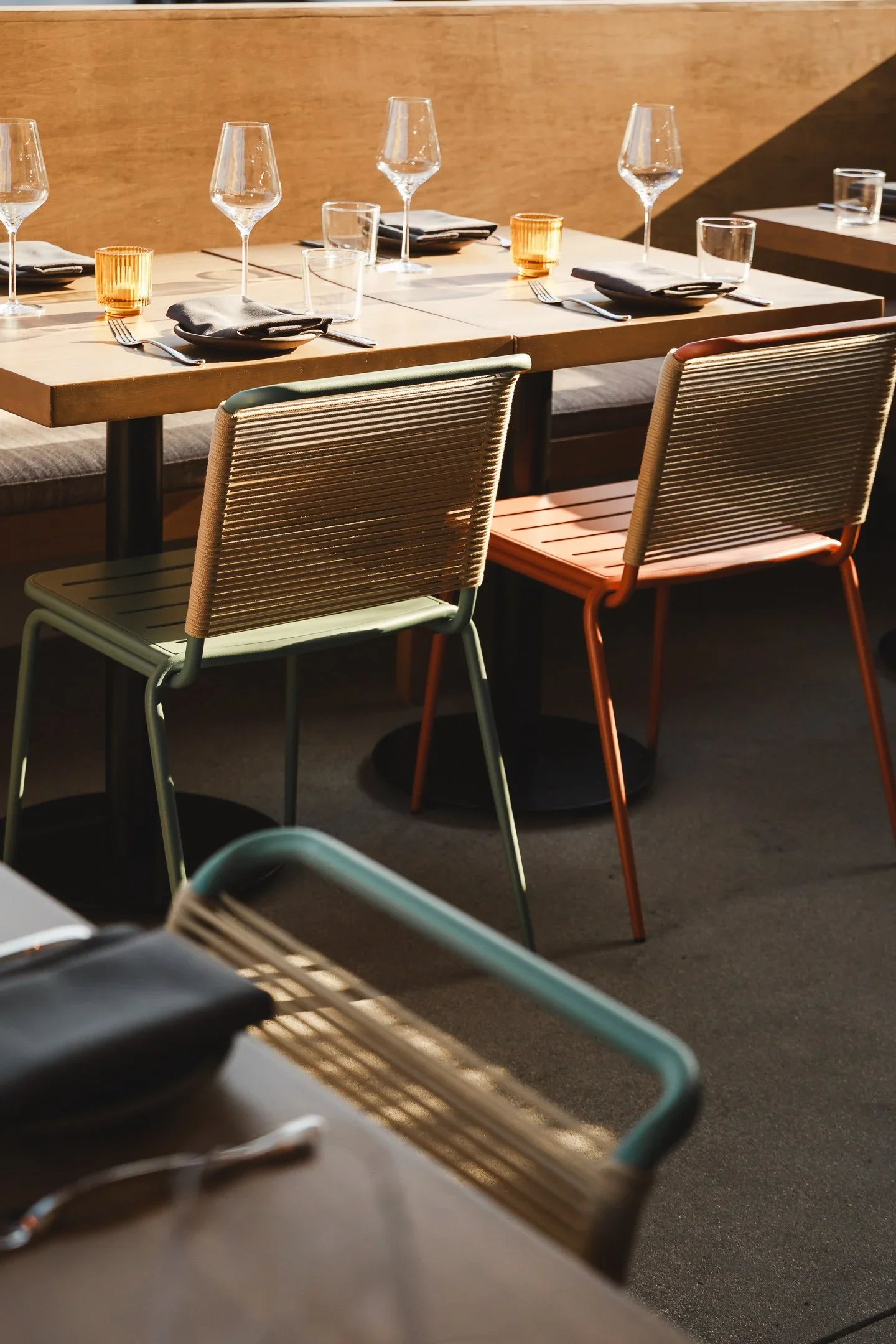 Close-up ofchair back against teal slatted banquette divider with set dining table in background — Marlena restaurant Long Beach by Mokume Design Studio