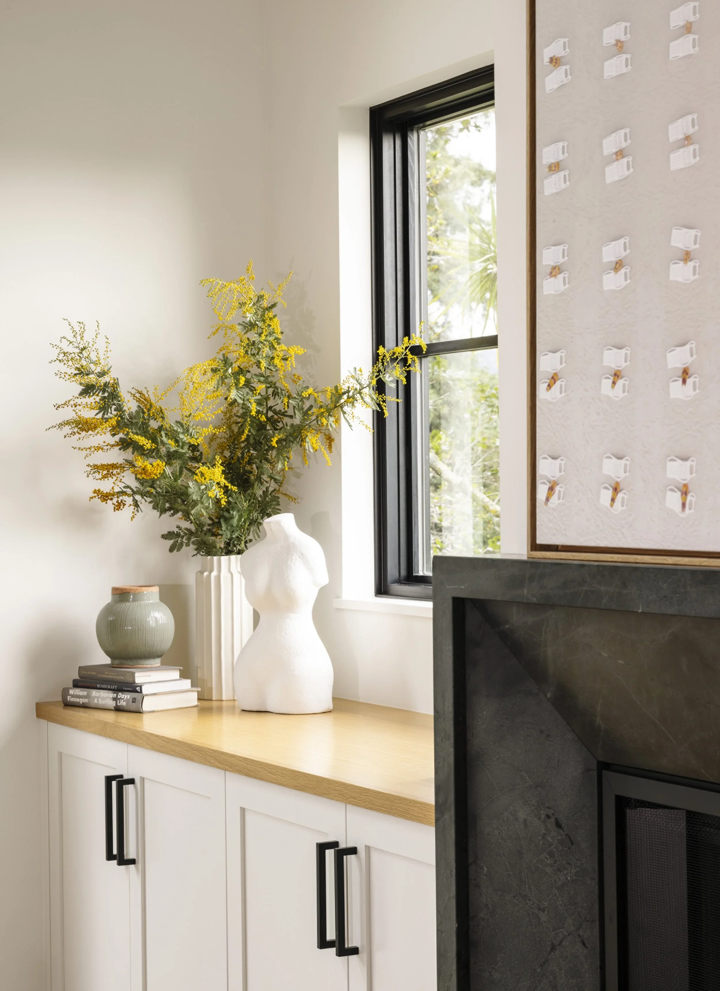White built-in cabinetry with oak countertop beside dark marble fireplace surround, styled with figurative ceramic vase and mimosa branches — Corte Madera Residence by Mokume Design Studio