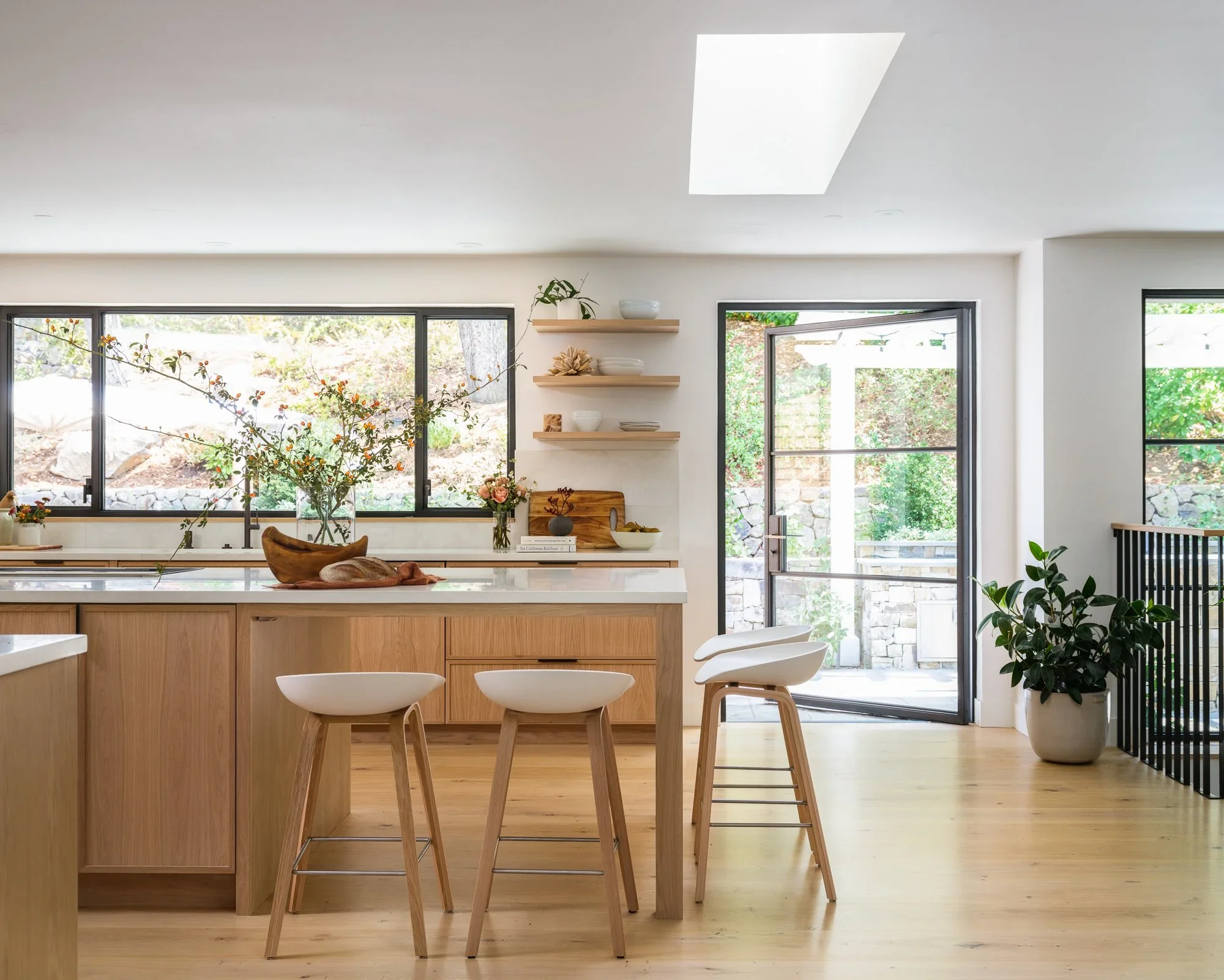 Open-concept natural oak kitchen with large waterfall island, white quartz countertops, black hardware, and skylight — Lafayette California home remodel by Mokume Design Studio