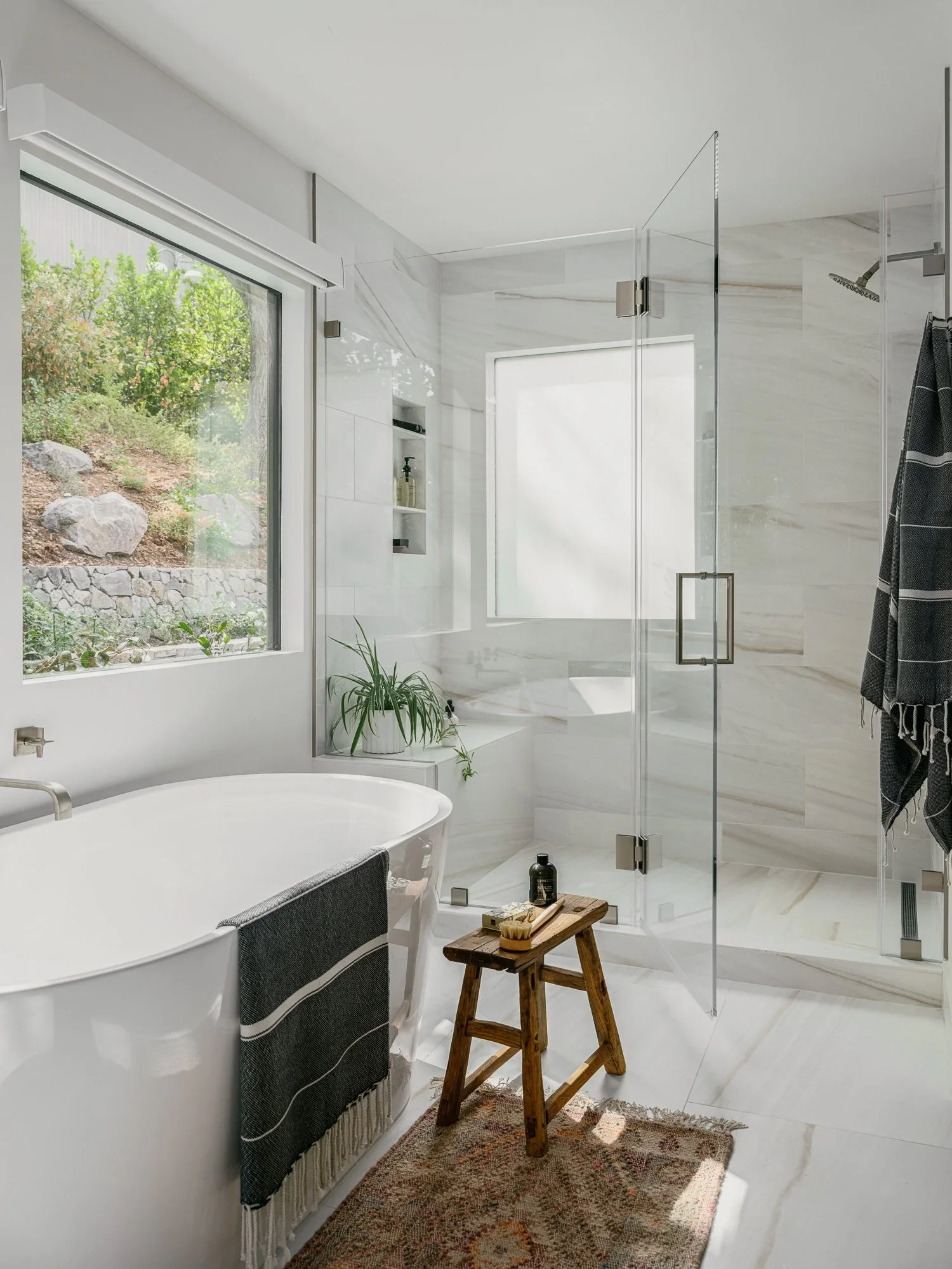 Primary bathroom with freestanding soaking tub, frameless glass walk-in shower, marble tile surround, and hillside views through black-framed windows — Lafayette California home remodel by Mokume Design Studio