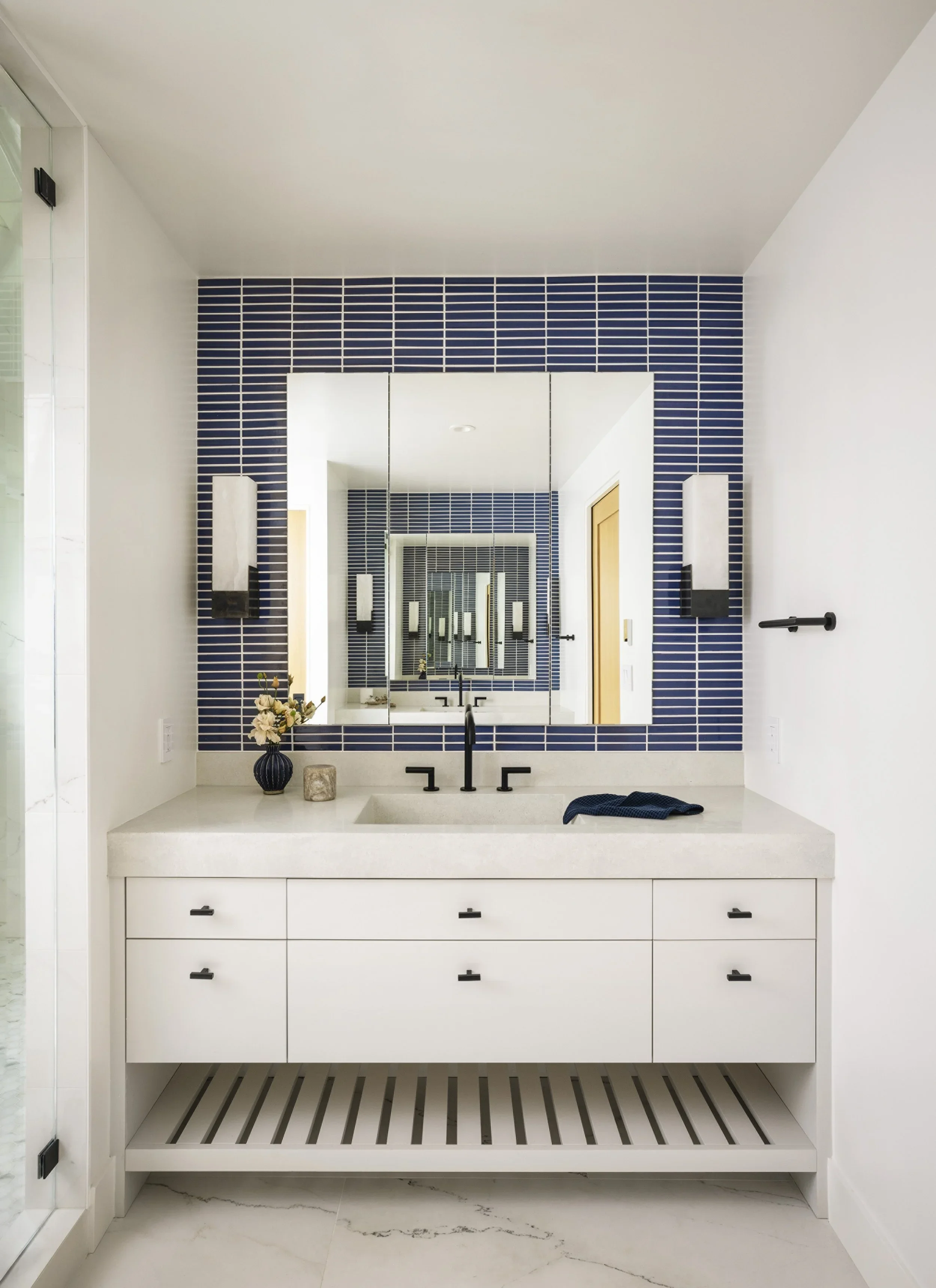 Primary bathroom vanity with white shaker cabinetry, concrete countertop, cobalt blue stacked tile accent wall framing medicine cabinet mirror, and black matte hardware — Corte Madera Residence by Mokume Design Studio