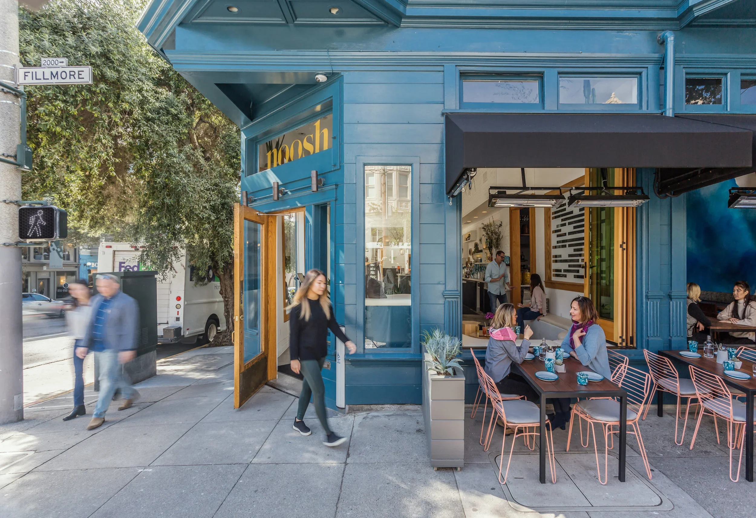 Noosh restaurant exterior on Fillmore Street San Francisco with blue painted facade, oak-framed entry, blush pink wire patio chairs, and open sidewalk seating — restaurant design by Mokume Design Studio