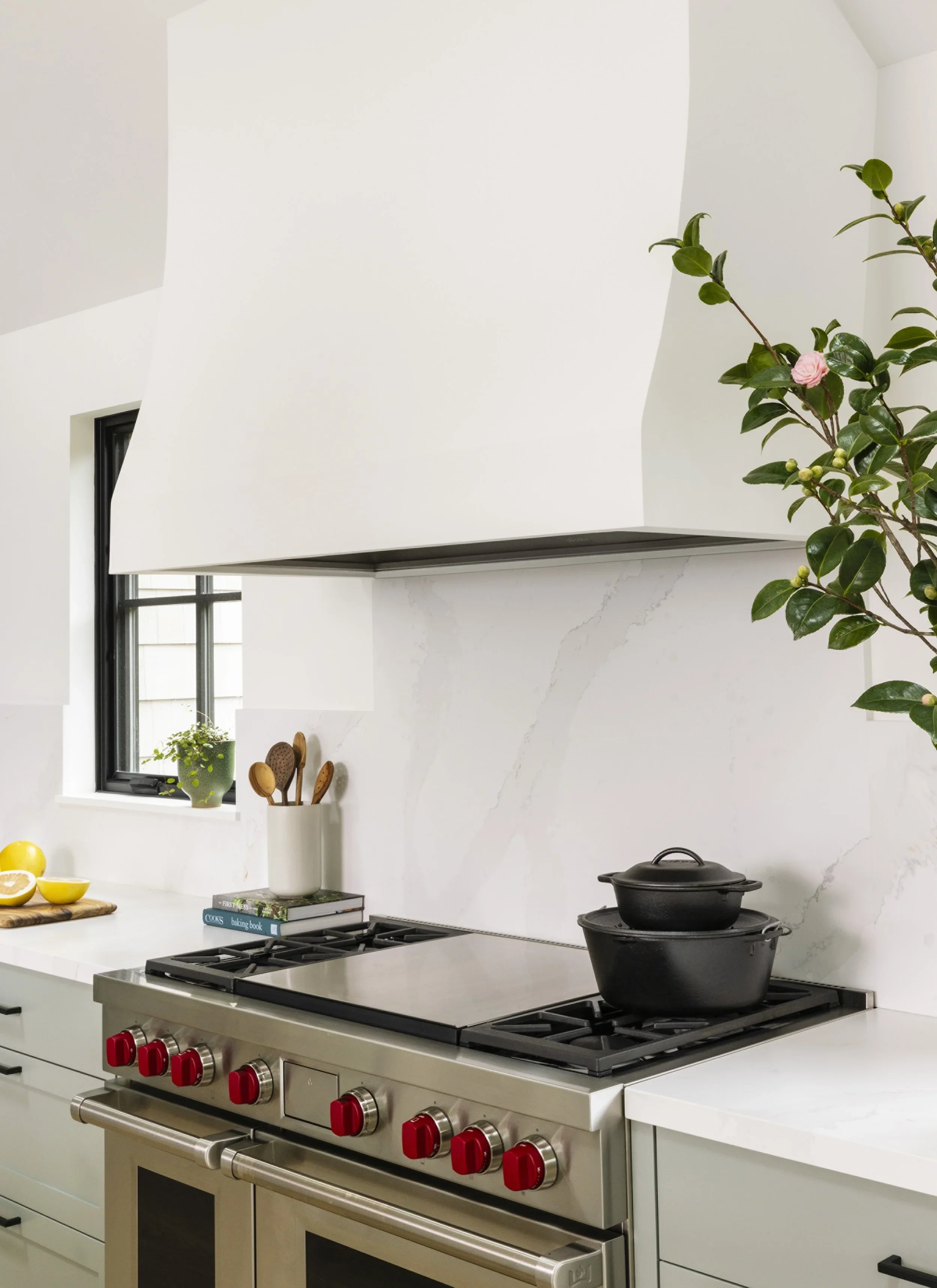 Wolf professional range with red knobs beneath oversized white plaster range hood and Calacatta marble slab backsplash — Corte Madera Residence by Mokume Design Studio