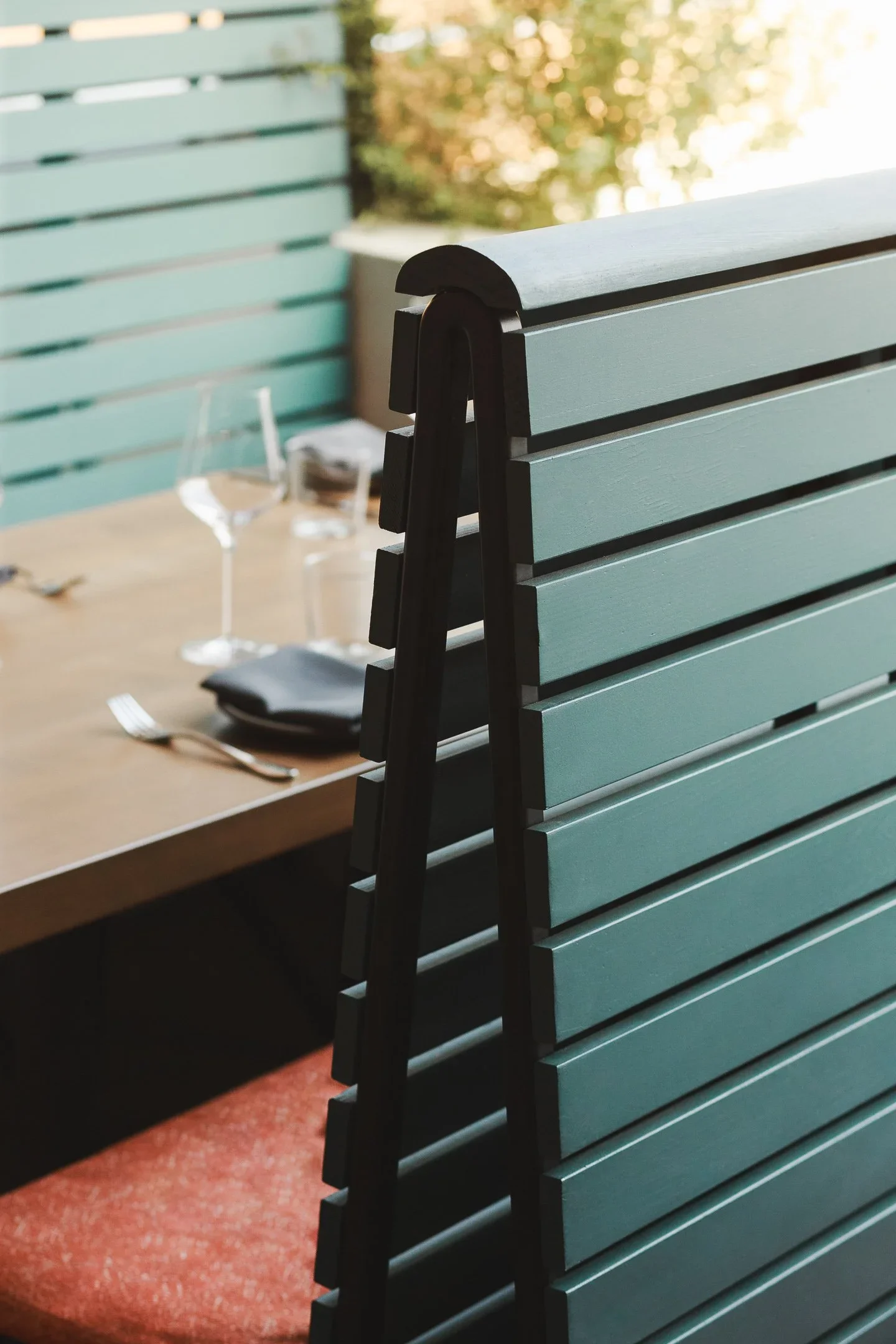 Close-up of custom chair back against teal slatted banquette divider with set dining table in background — Marlena restaurant Long Beach by Mokume Design Studio