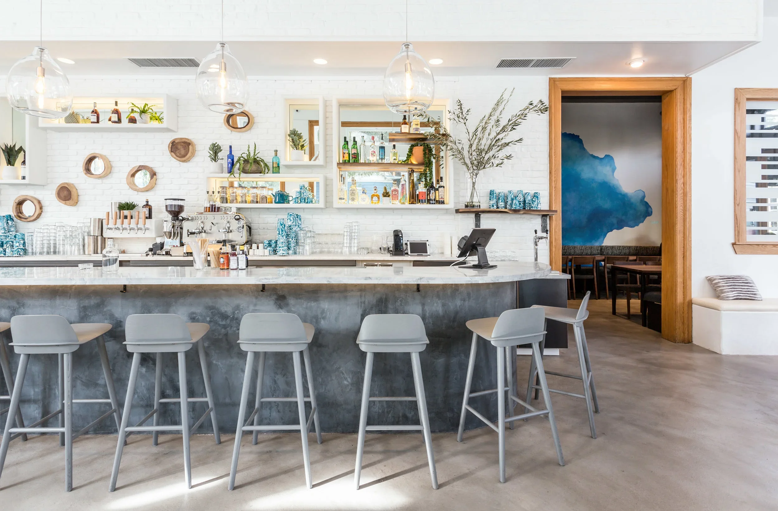 Noosh restaurant bar with polished concrete base, marble countertop, globe glass pendants, white painted brick wall, and blue watercolor mural — Fillmore Street San Francisco restaurant design by Mokume Design Studio