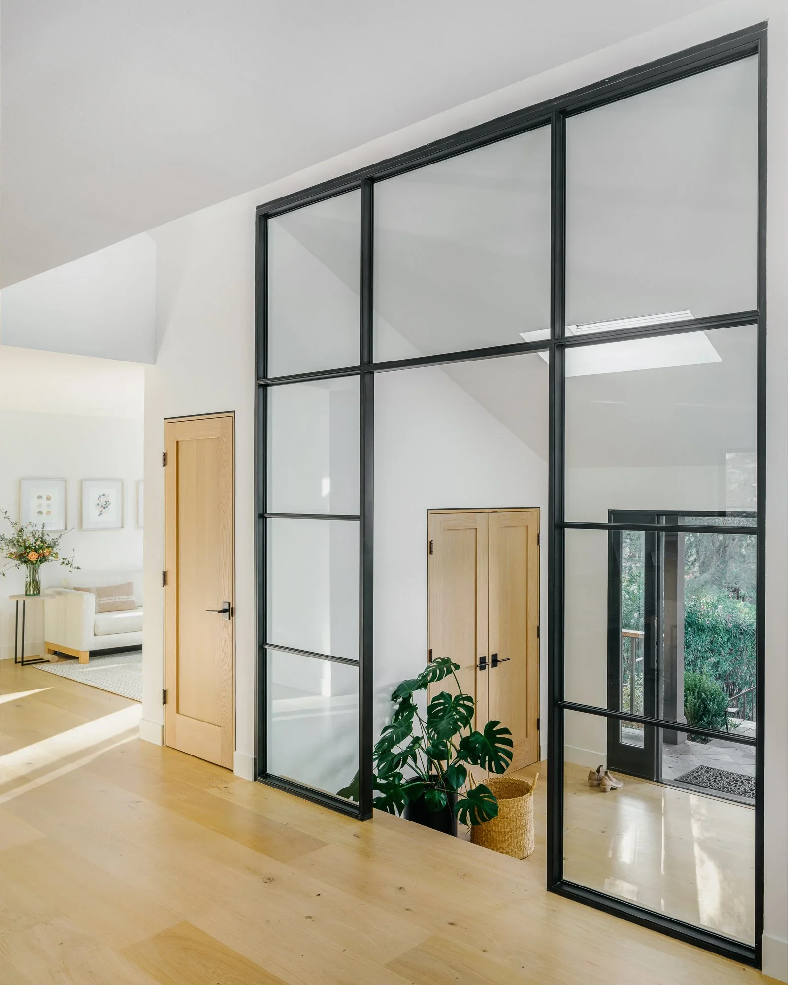 Natural oak kitchen island with white quartz waterfall countertop, open wood shelving, skylight, and steel-framed glass door opening to hillside terrace — Lafayette California home remodel by Mokume Design Studio