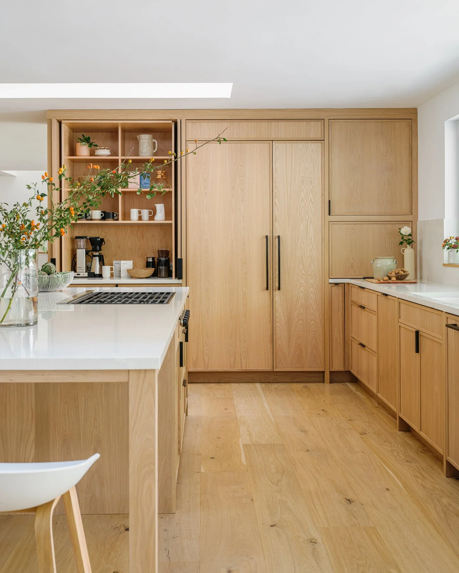Open-concept natural oak kitchen with large waterfall island, white quartz countertops, black hardware, and skylight — Lafayette California home remodel by Mokume Design Studio