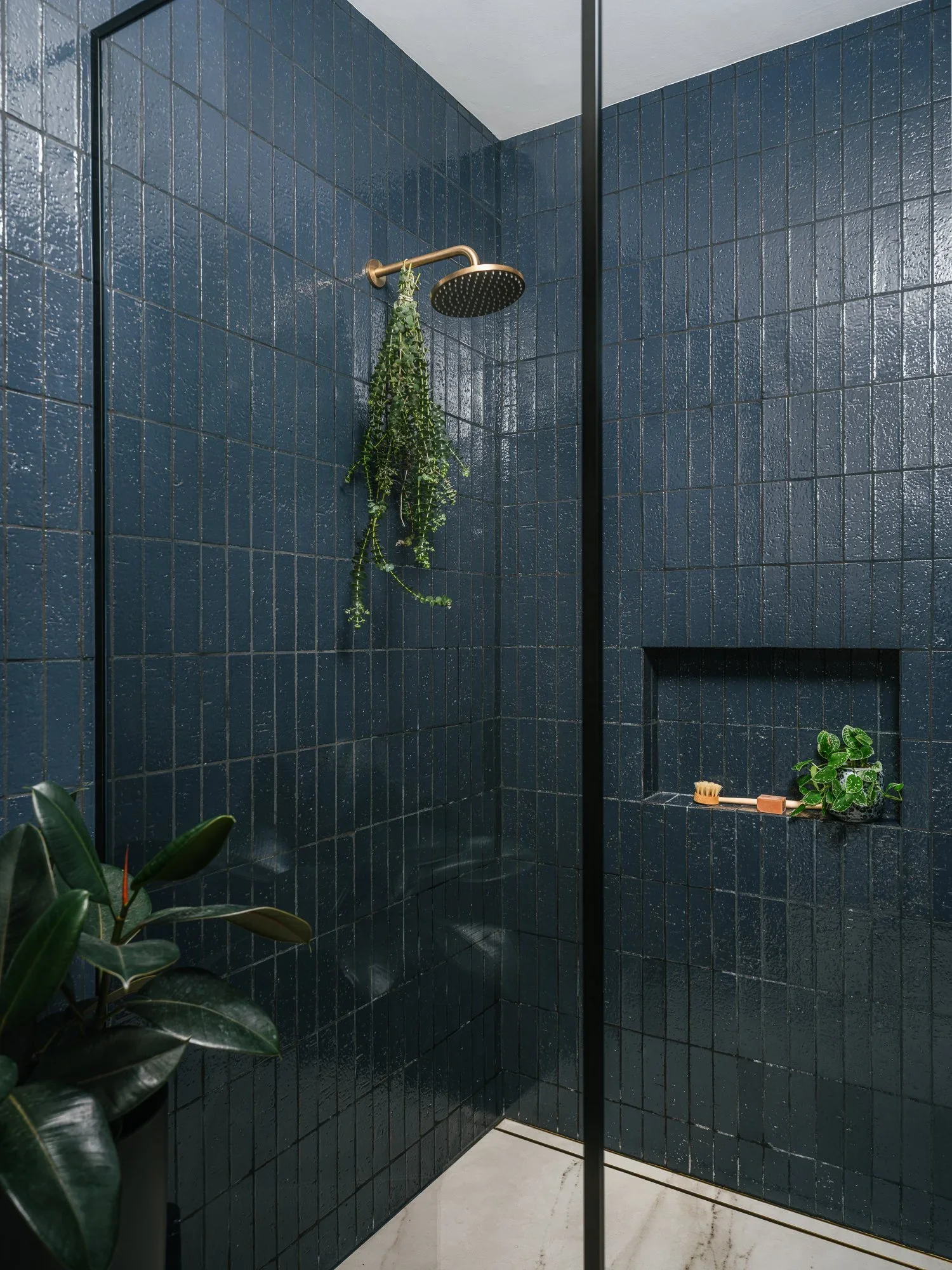 Floor-to-ceiling navy glazed ceramic tile walk-in shower with brass rain showerhead, built-in niche, and hanging eucalyptus — Hill Street Residence San Francisco by Mokume Design Studio