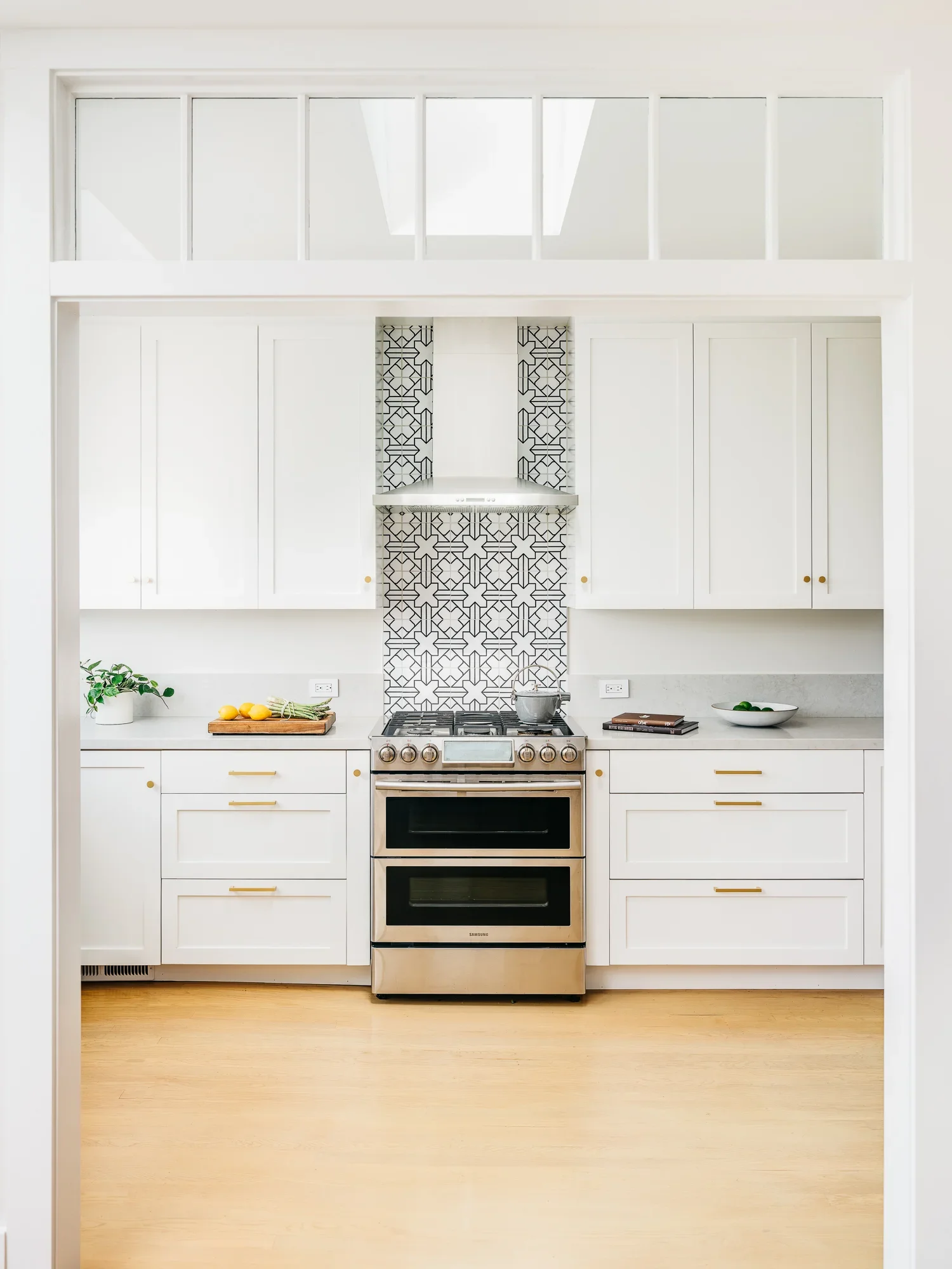 White shaker kitchen with gold hardware, stainless steel double oven range, and bold black-and-white geometric tile backsplash — modern California kitchen remodel by Mokume Design Studio