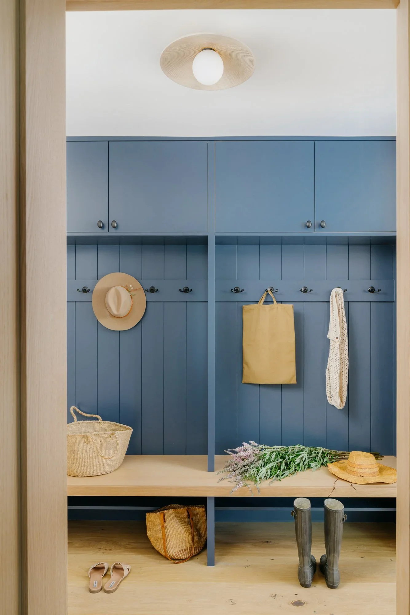 Built-in mudroom with dusty blue shiplap cabinetry, black coat hooks, natural oak bench, and woven pendant light — Lafayette California home remodel by Mokume Design Studio