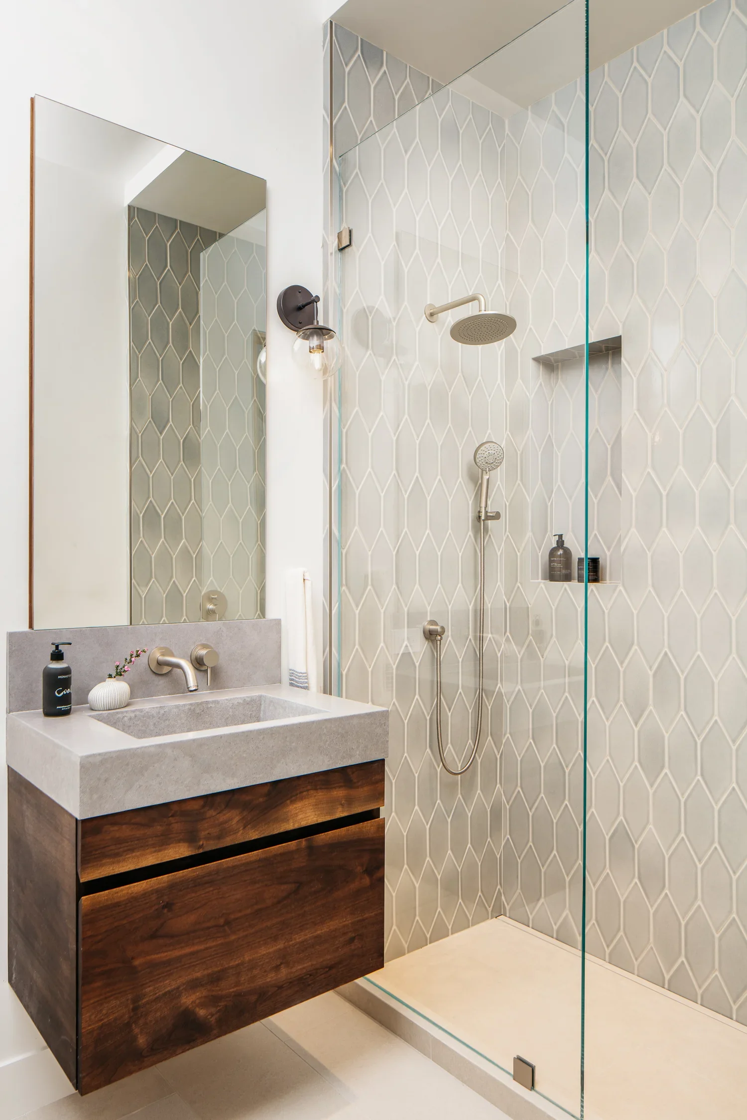 Modern bathroom with floating walnut vanity, honed concrete vessel sink, elongated hexagon tile shower surround, and frameless glass enclosure — Mission Loft San Francisco by Mokume Design Studio