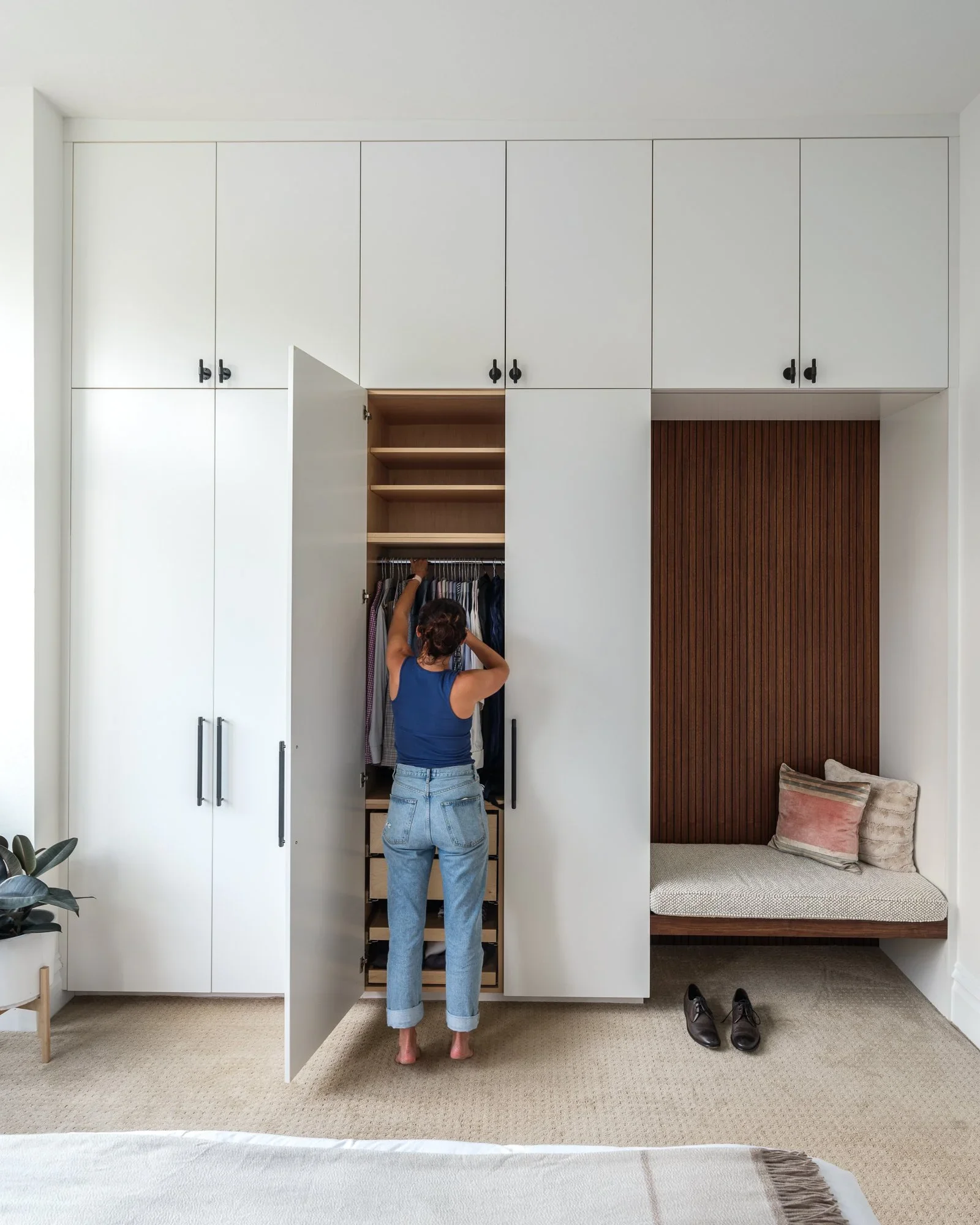 Floor-to-ceiling white built-in wardrobe with black hardware, integrated walnut slatted reading nook with upholstered bench, and oak interior shelving — Pacific Heights San Francisco by Mokume Design Studio