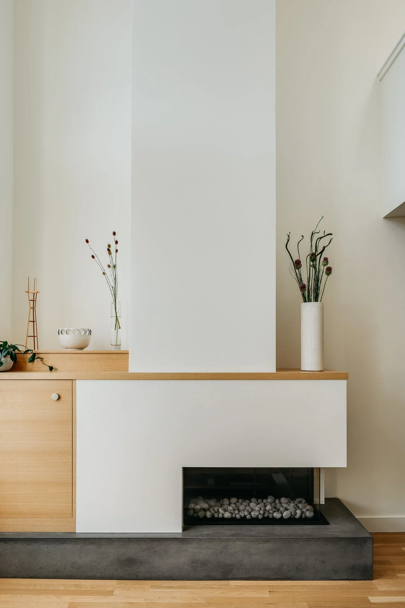 Minimalist concrete and white plaster fireplace surround with natural oak built-in cabinetry and sculptural dried botanicals — Nopa Loft San Francisco by Mokume Design Studio