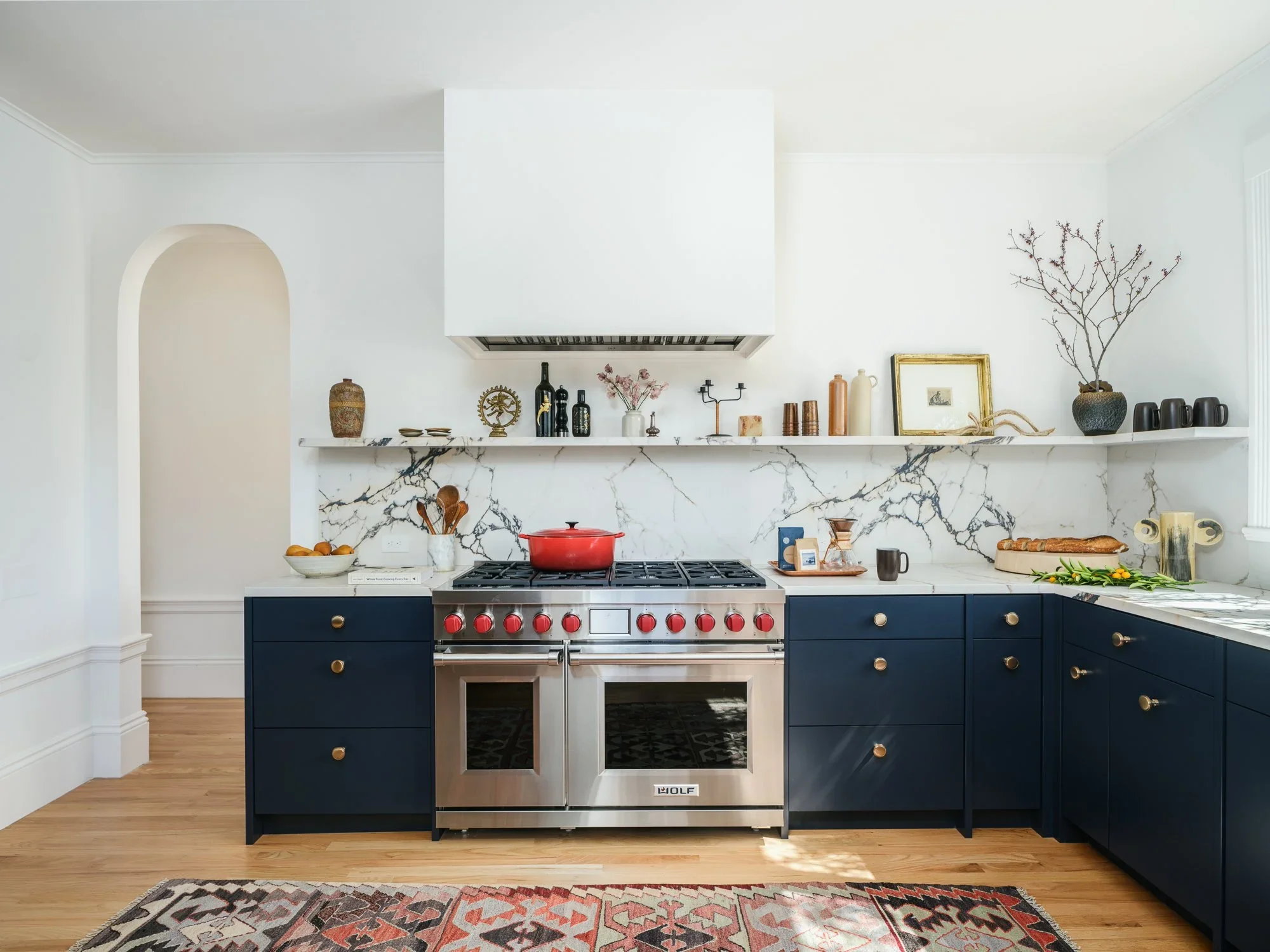 Navy blue shaker kitchen with Calacatta marble backsplash, Wolf professional range, brass hardware, open shelving, and Kilim rug on wide plank hardwood floors — Hill Street Residence San Francisco by Mokume Design Studio