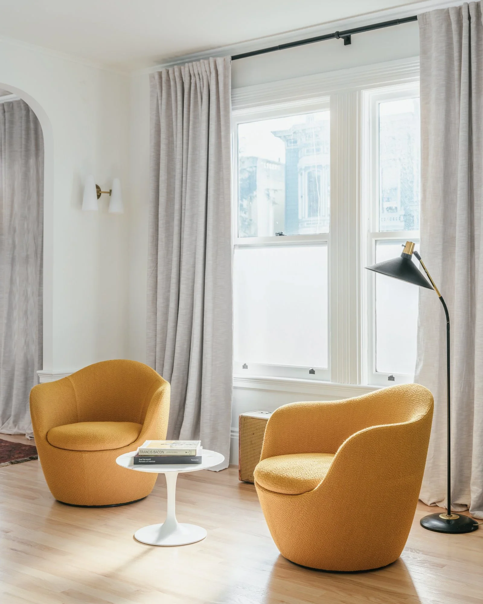 Pair of mustard yellow bouclé swivel chairs flanking a Saarinen tulip side table beside floor-to-ceiling linen drapes and black floor lamp — Hill Street Residence San Francisco by Mokume Design Studio
