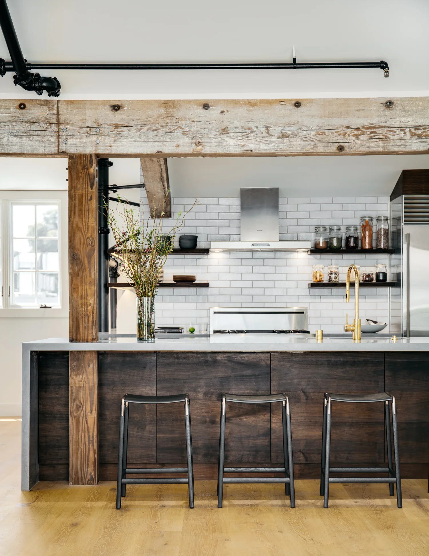 Industrial loft kitchen with dark walnut island, concrete countertop, gold faucet, white subway tile backsplash, open shelving, and exposed reclaimed wood beams — Mission Loft San Francisco by Mokume Design Studio