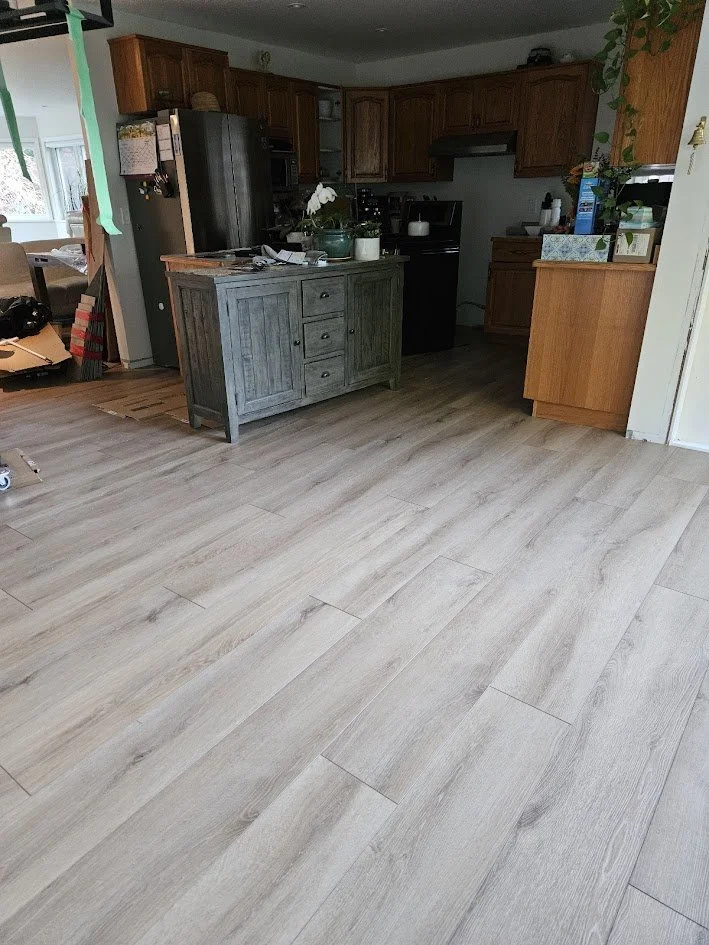 Open kitchen with wooden cabinets, black appliances, and a countertop island with plants and papers.