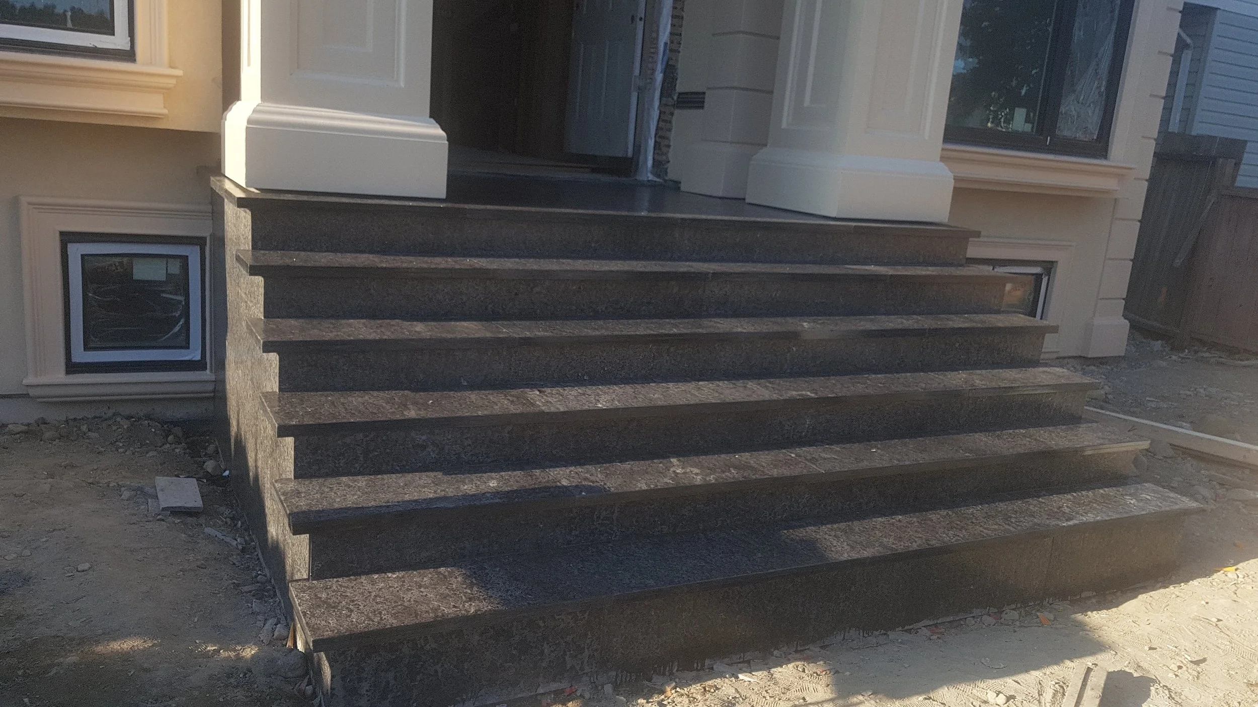 Black granite steps leading to the front door of a house, with a white door frame and surrounding beige plaster walls.