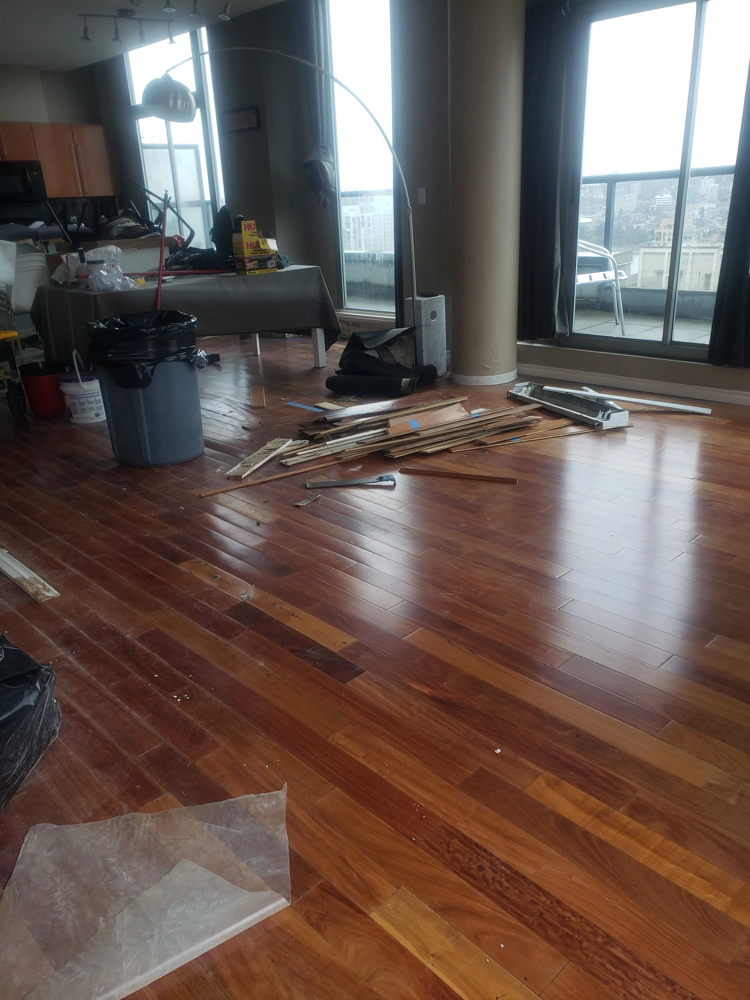 Living room with hardwood floors, clutter, and tools, next to a large window and balcony.