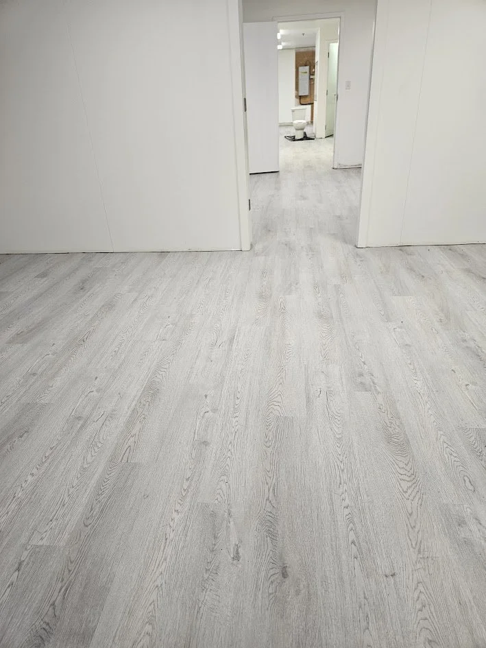 Interior of a room with light-colored wooden floor, white walls, and an open doorway leading to a bathroom with a white toilet and a mirror.