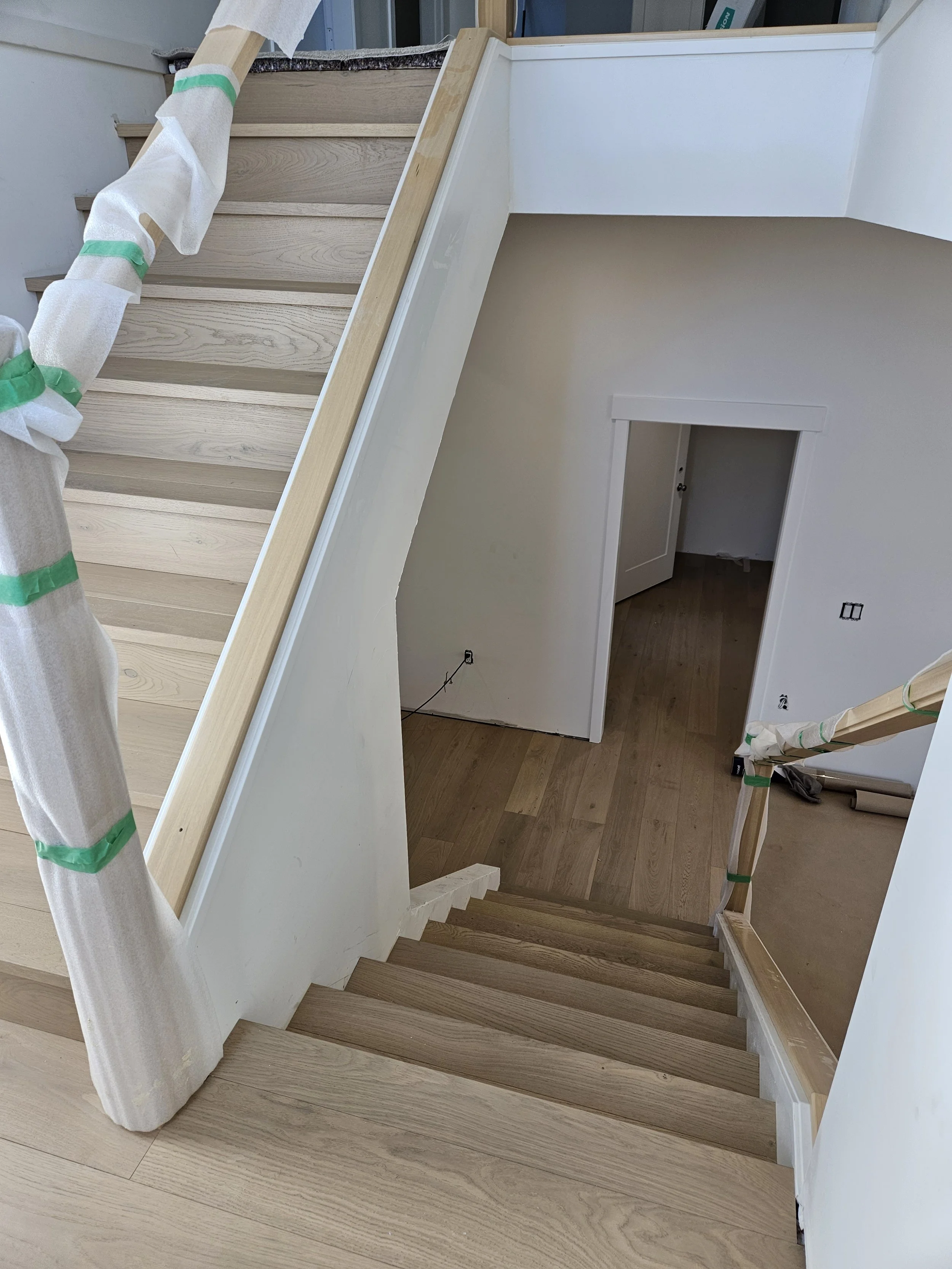 Interior view of a staircase under construction with wood steps and unfinished areas, including tape and protective wrapping on the handrail.