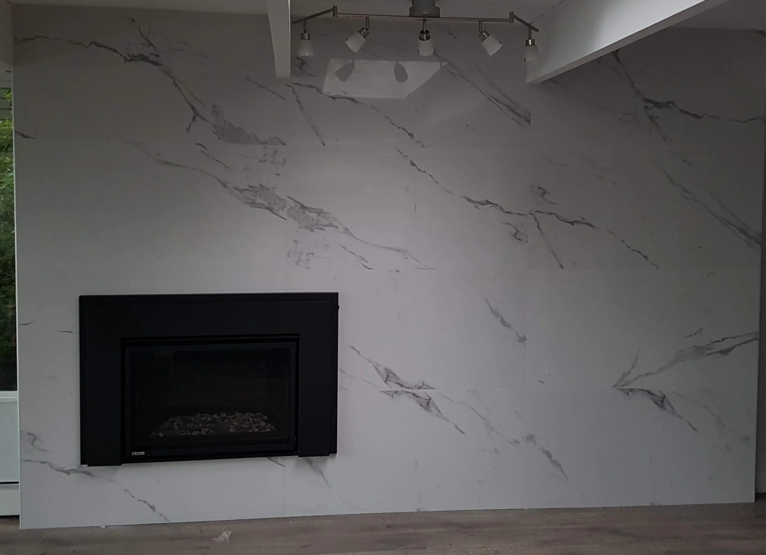 Modern living room with large white marble wall featuring gray veining and a black fireplace insert.