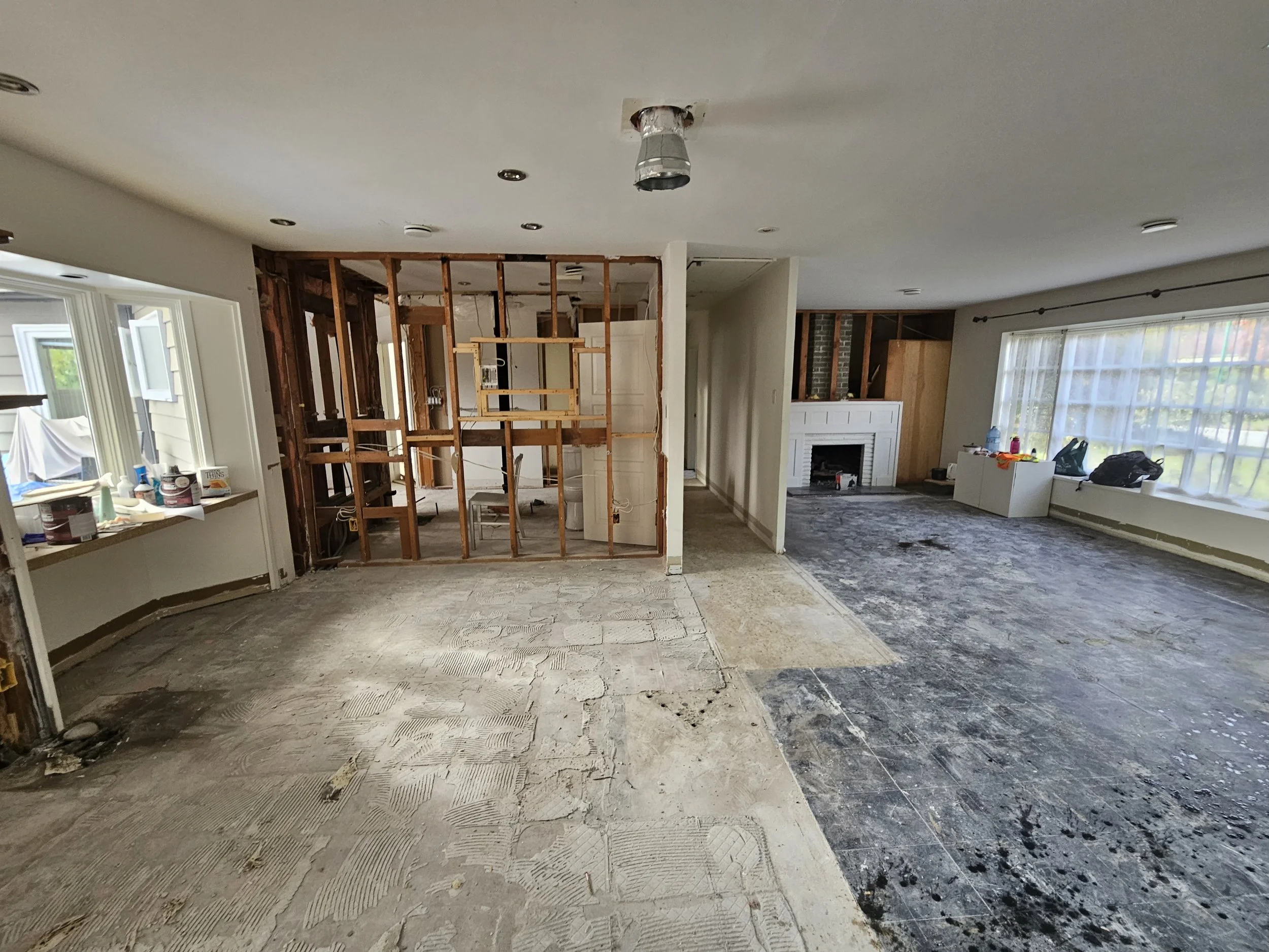 Living room undergoing renovation with partially removed flooring, exposed framing, and a white fireplace.