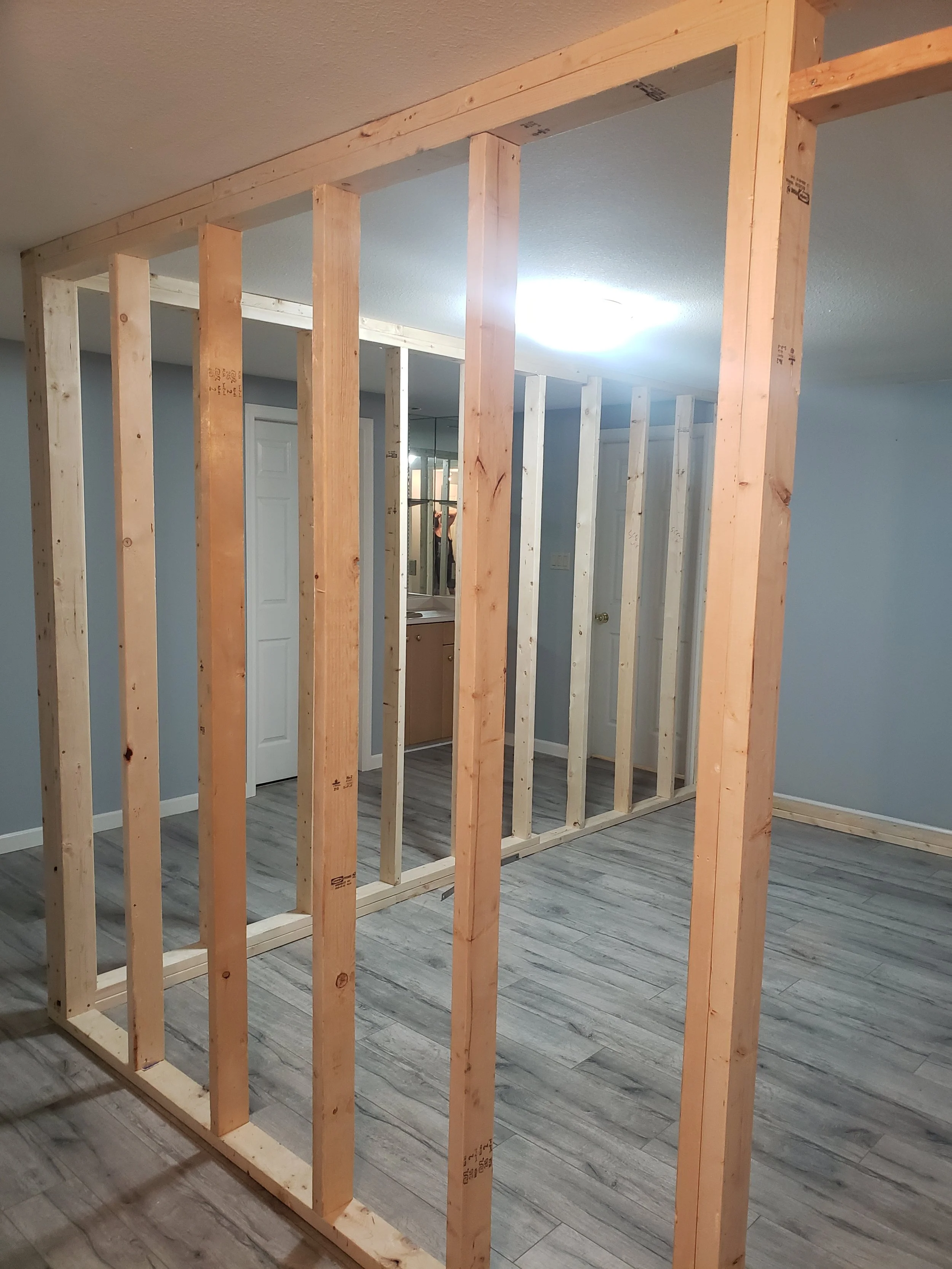 Framing for a wall construction in an indoor space, with visible wooden studs and a ceiling light.