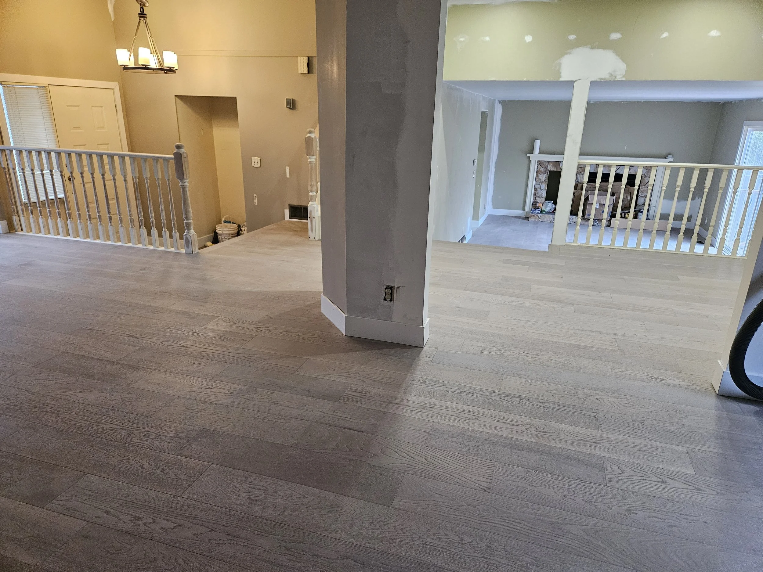 Interior view of a house under renovation, showing unfinished walls, wood flooring, a fireplace, and railings.