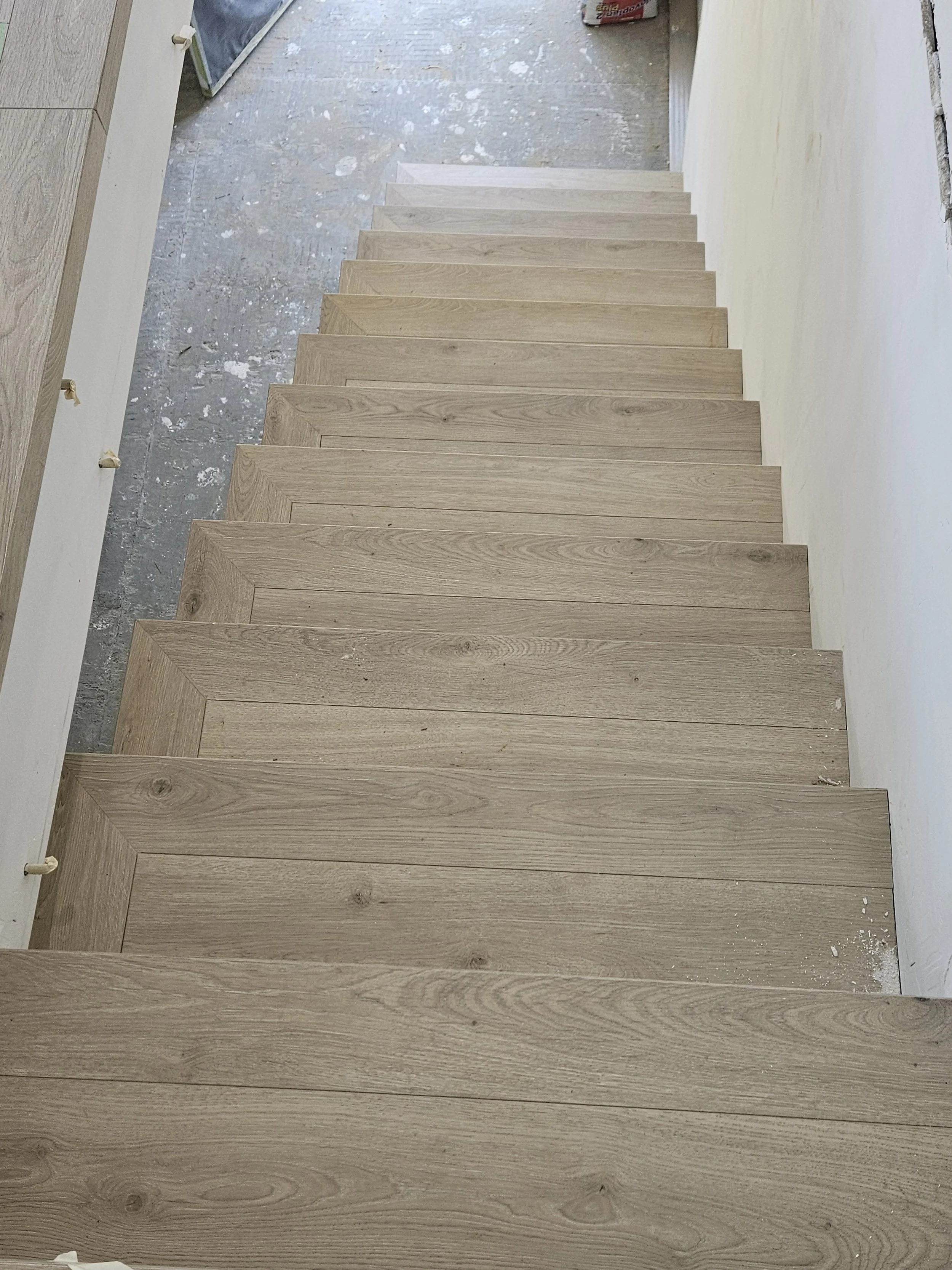 A straight staircase with wooden steps in a construction or renovation site, with some construction debris on the floor and partially finished walls.