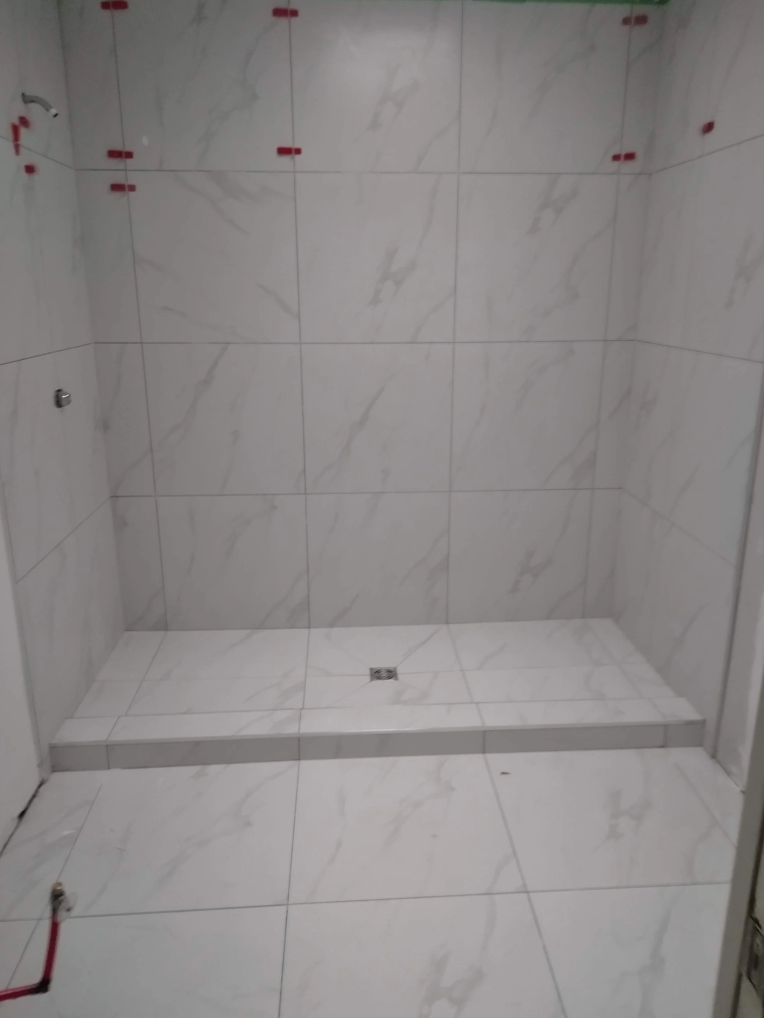 Empty shower area with white marble tiles, a floor drain, and plumbing fixtures, ready for installation.