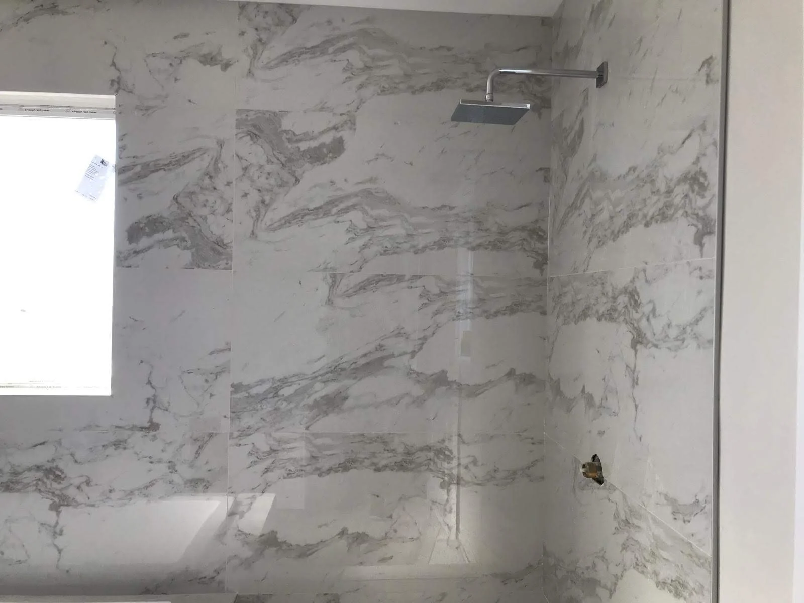 A bathroom shower area with marble tiles and a rain shower head, no fixtures installed yet.