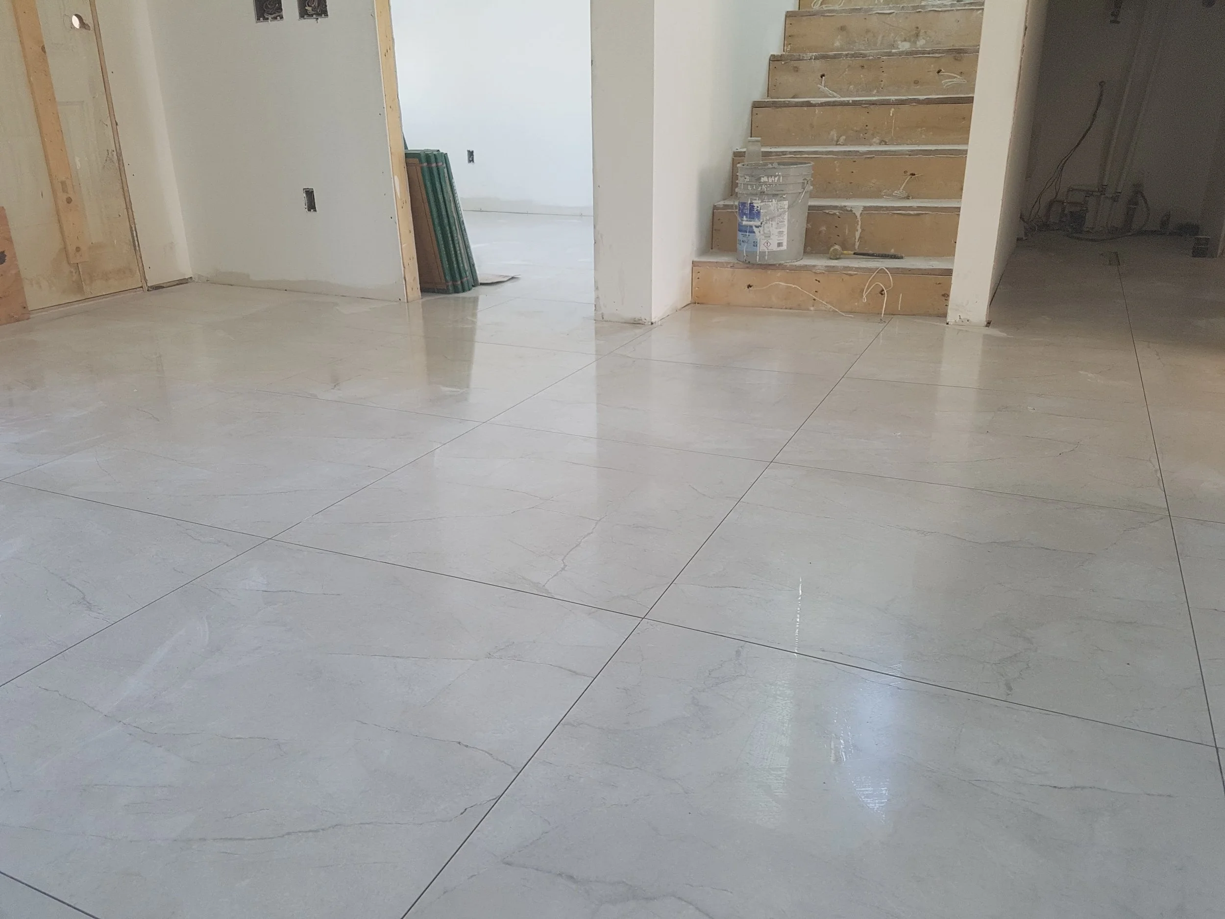 Finished marble tile flooring in a residential interior with an open hallway leading to a staircase under construction.