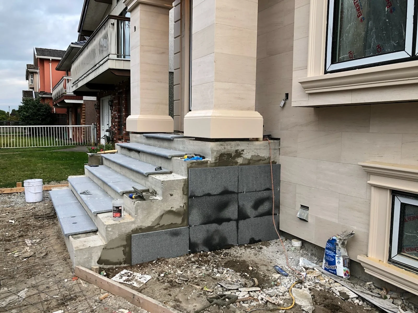 Construction site with brick stairs and beige house exterior, with ongoing work and construction materials around.