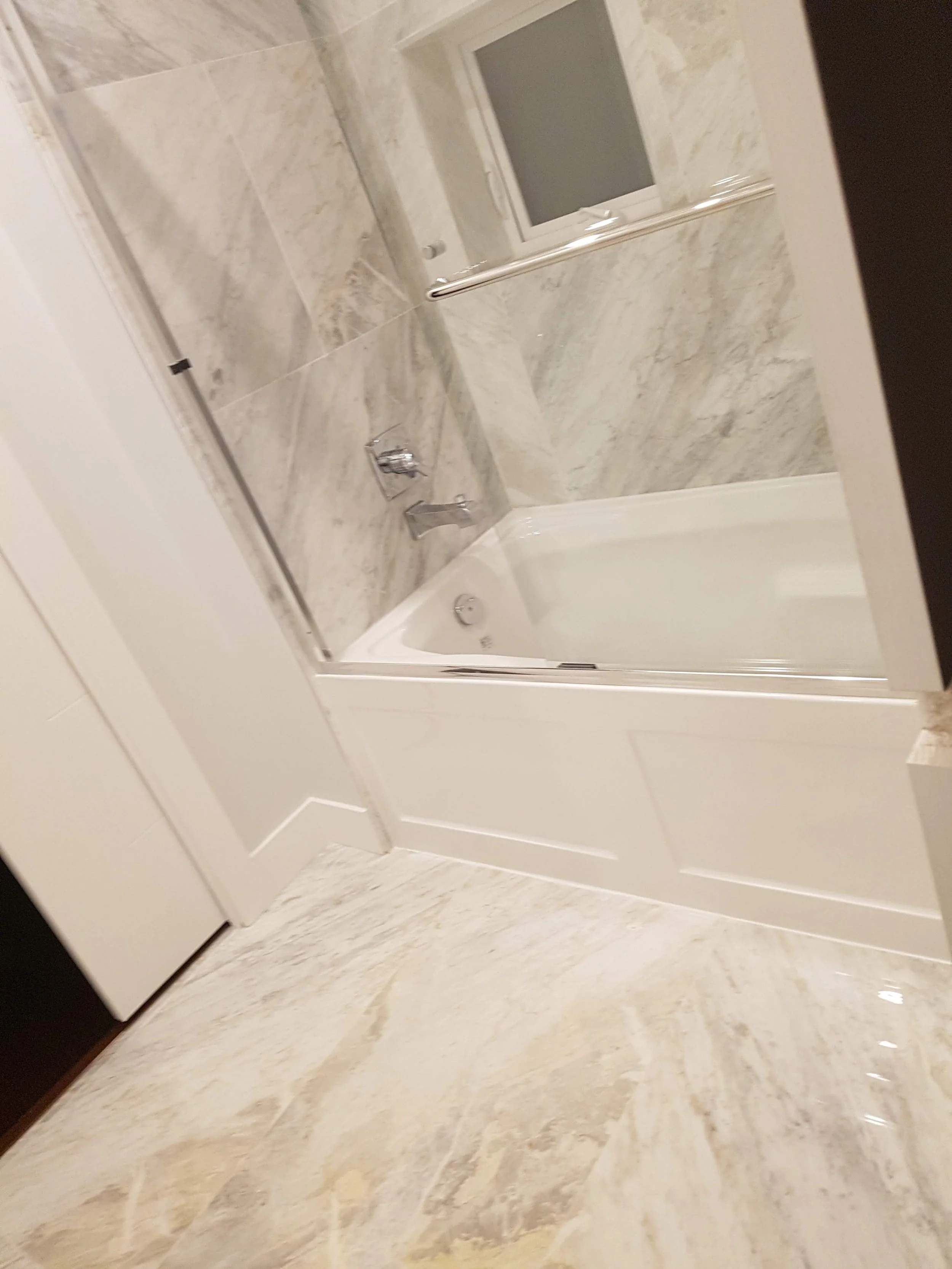 Bathroom with a bathtub and marble walls, a small window, and a glass shower enclosure.