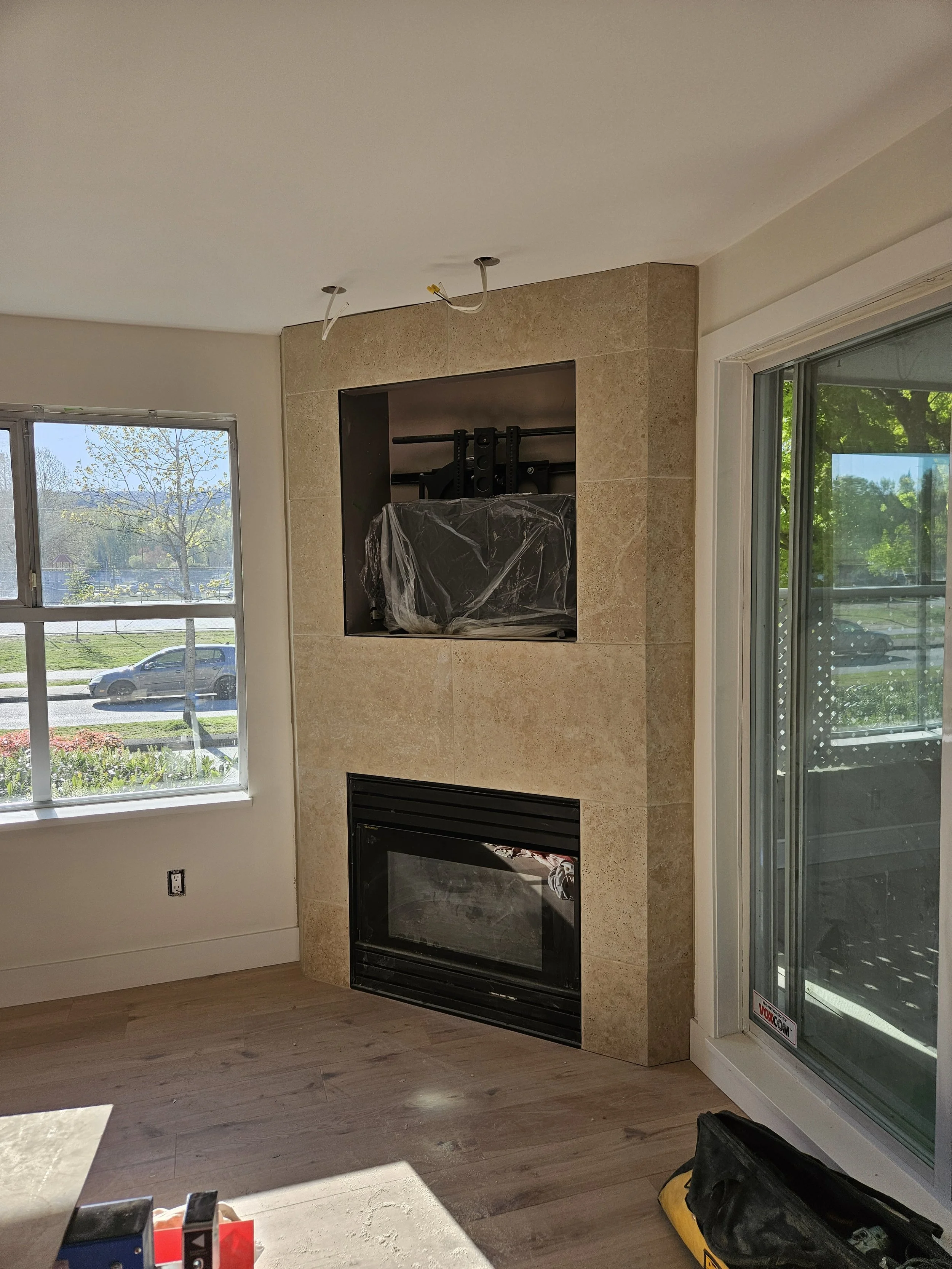 Living room with fireplace under construction, window to the left, sliding door to the right, and various tools and materials on the floor.
