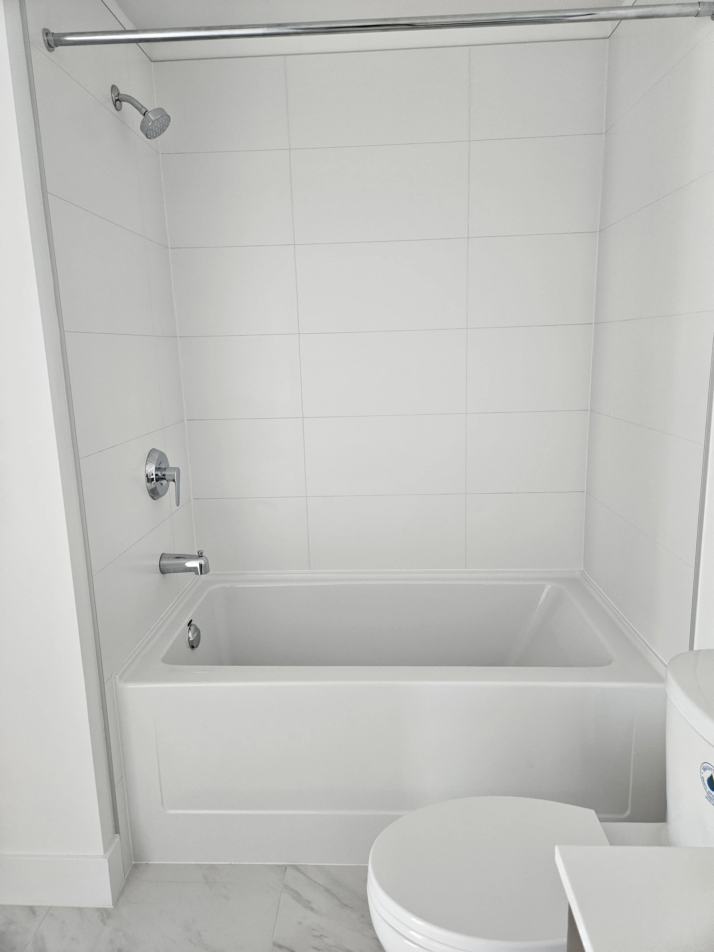 Bathroom with a white bathtub, wall-mounted showerhead, faucet, and control handle, white tile walls, and marble floor.