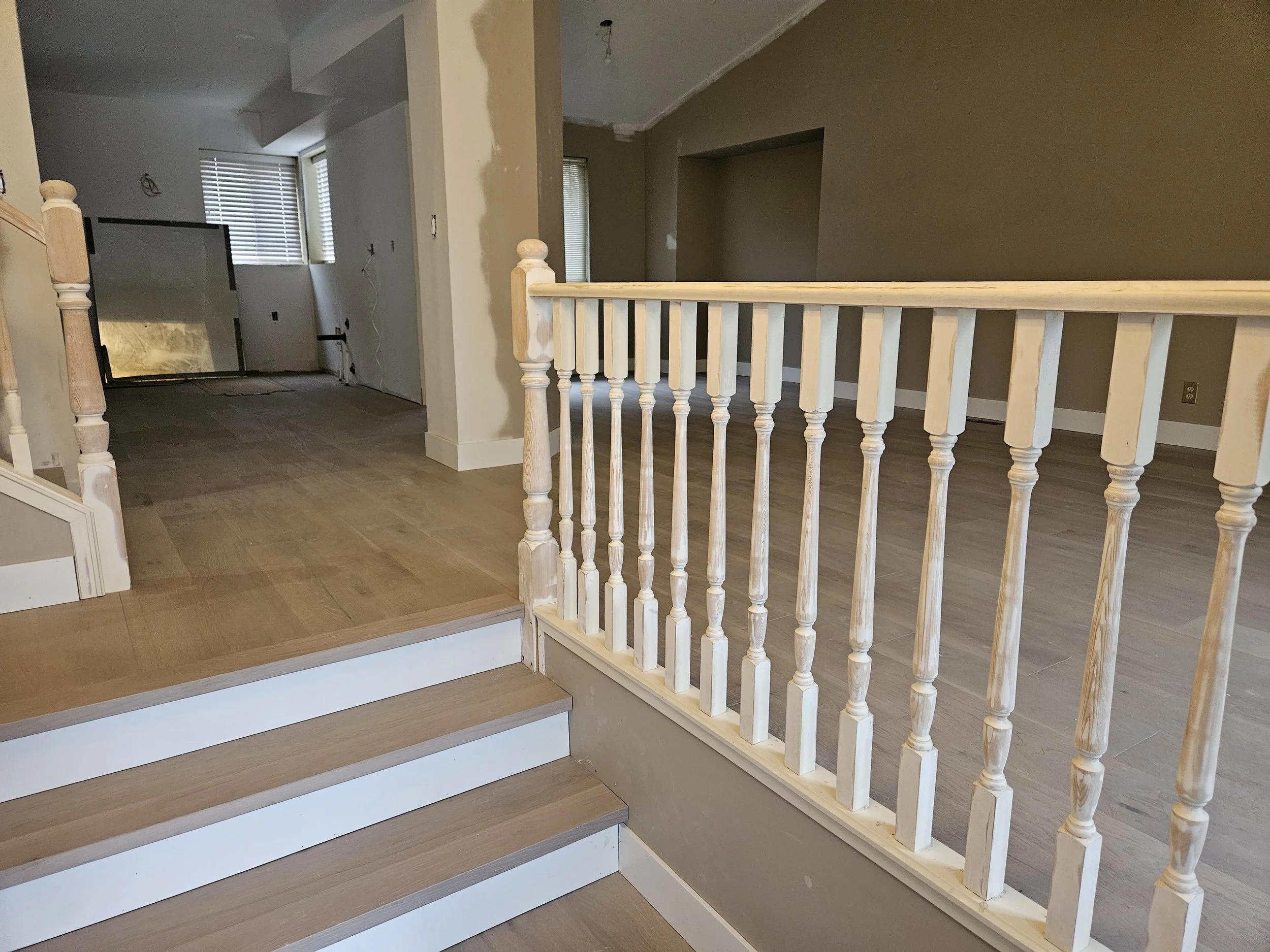Interior of a house under renovation showing stairs with white risers and wooden treads, a new white wooden banister, and unfinished walls with visible drywall and wiring.