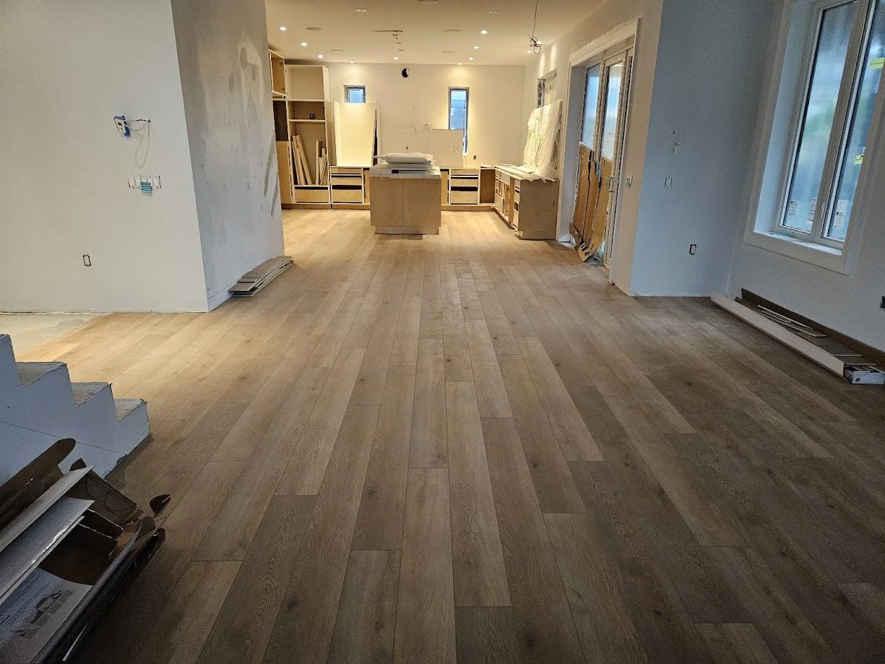 Living room under renovation with hardwood flooring, construction materials, and unfinished built-in shelves in the background.