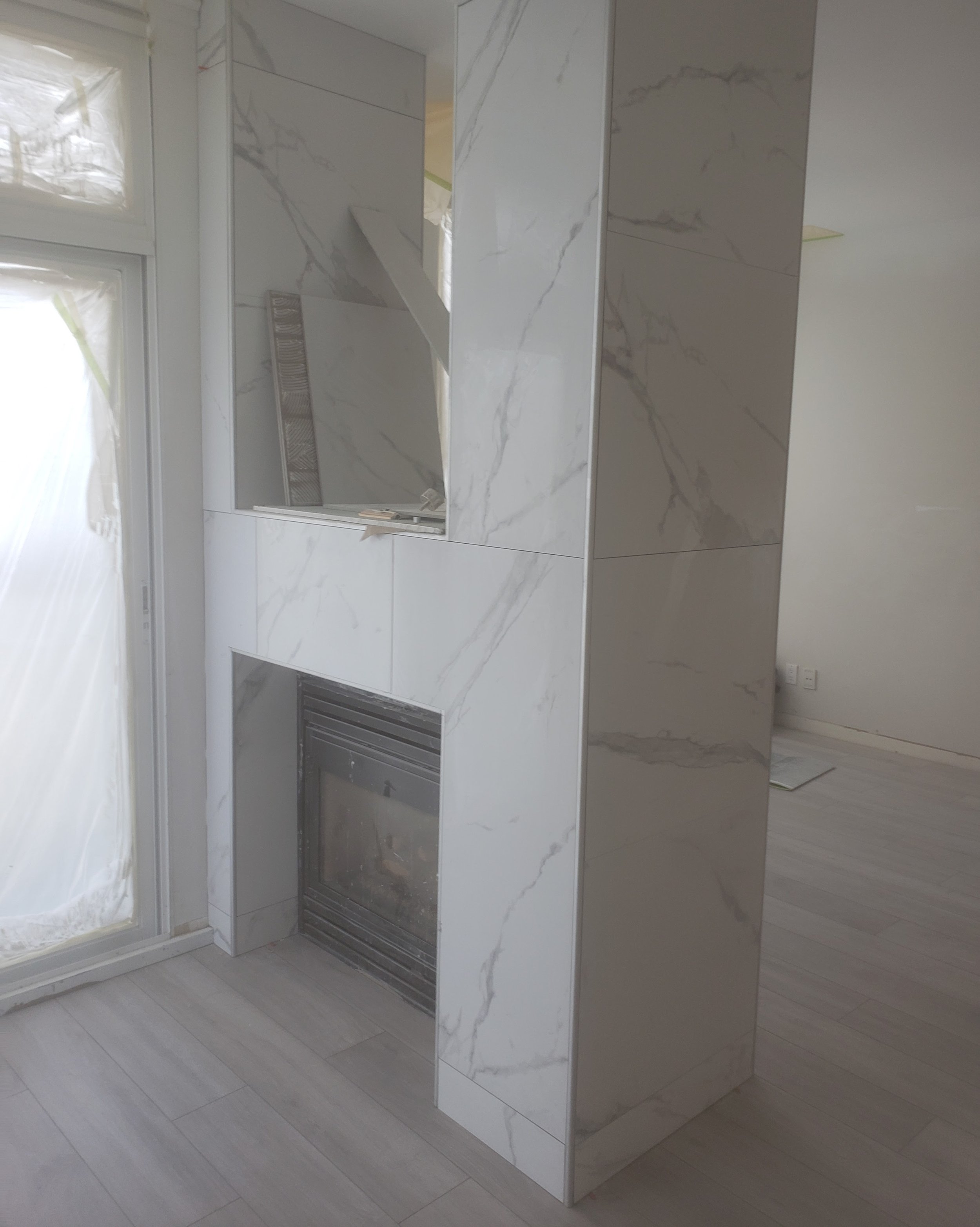 Marble fireplace with a built-in black metal vent and a small window with sunlight.