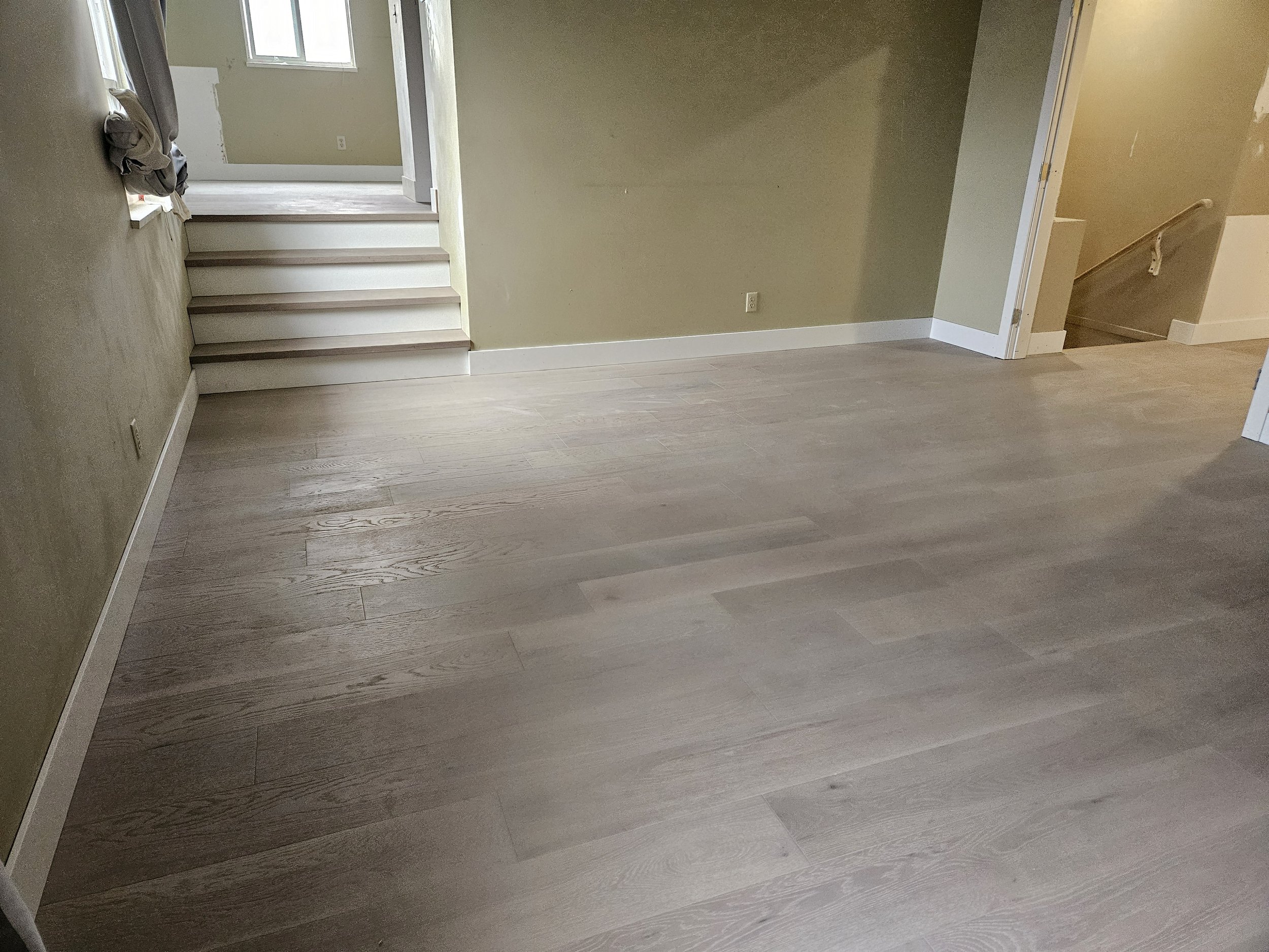 Empty room with light-colored hardwood floor, beige walls, staircase leading up on the left, and doorway on the right.