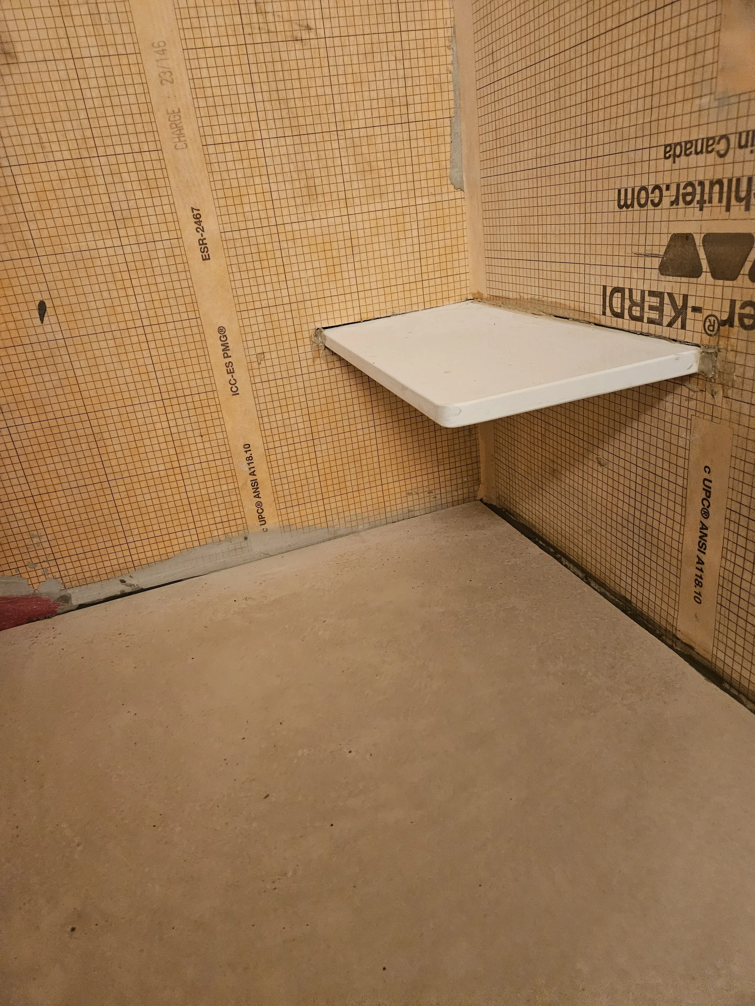Small white ceramic shelf attached to a bathroom wall with orange tile under construction.