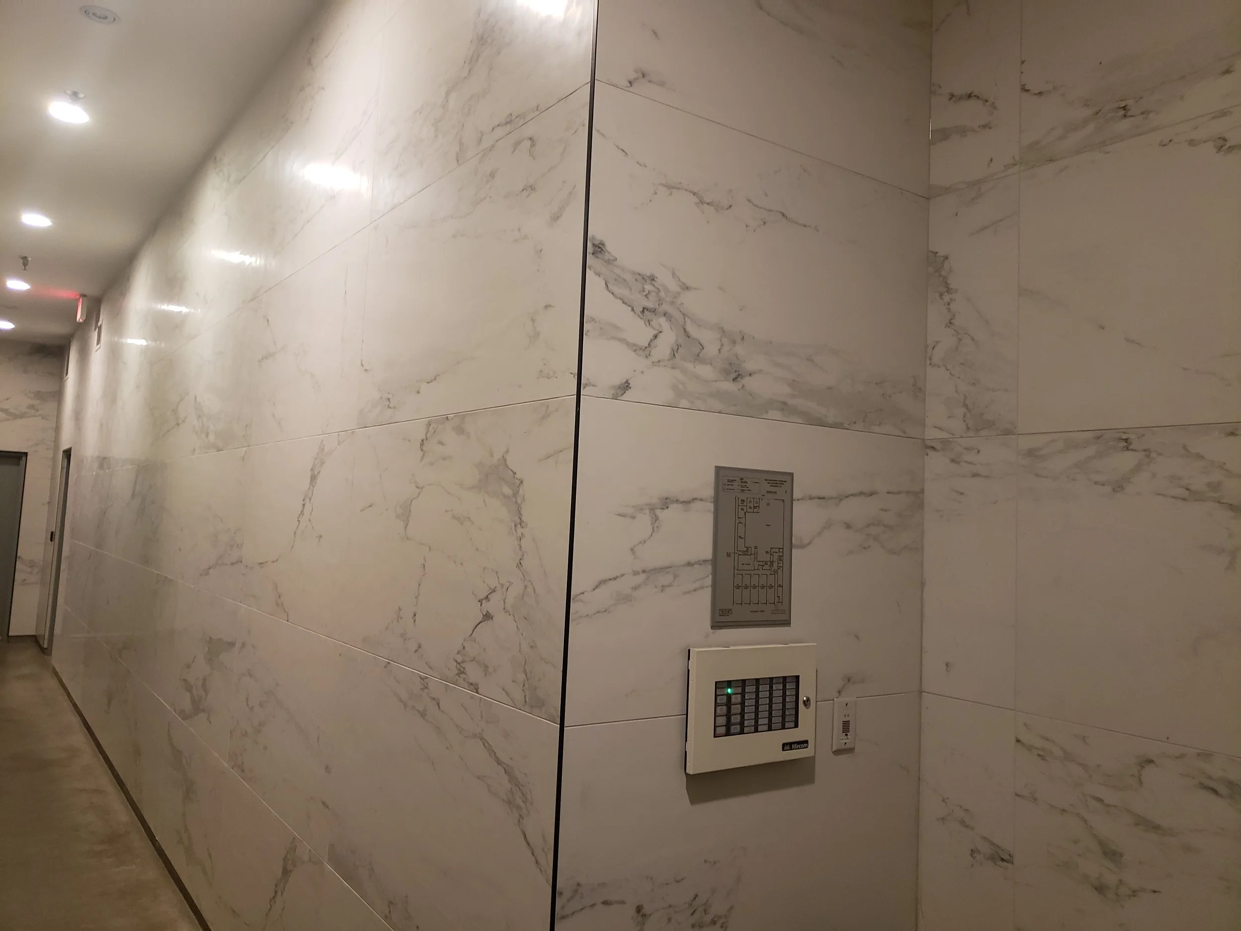 Marble tiled wall in a building hallway, with an elevator control panel and emergency telephone.