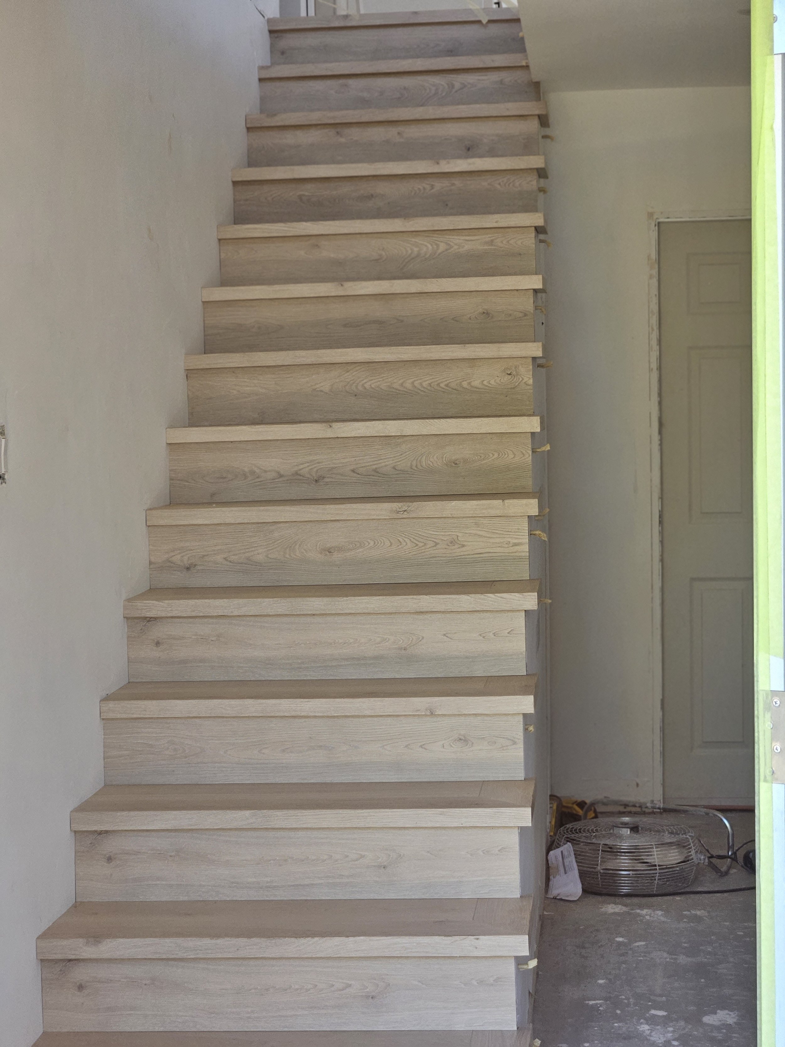 Photo of unfinished wooden stairs in progress of construction, inside a house with some construction tools and materials nearby.